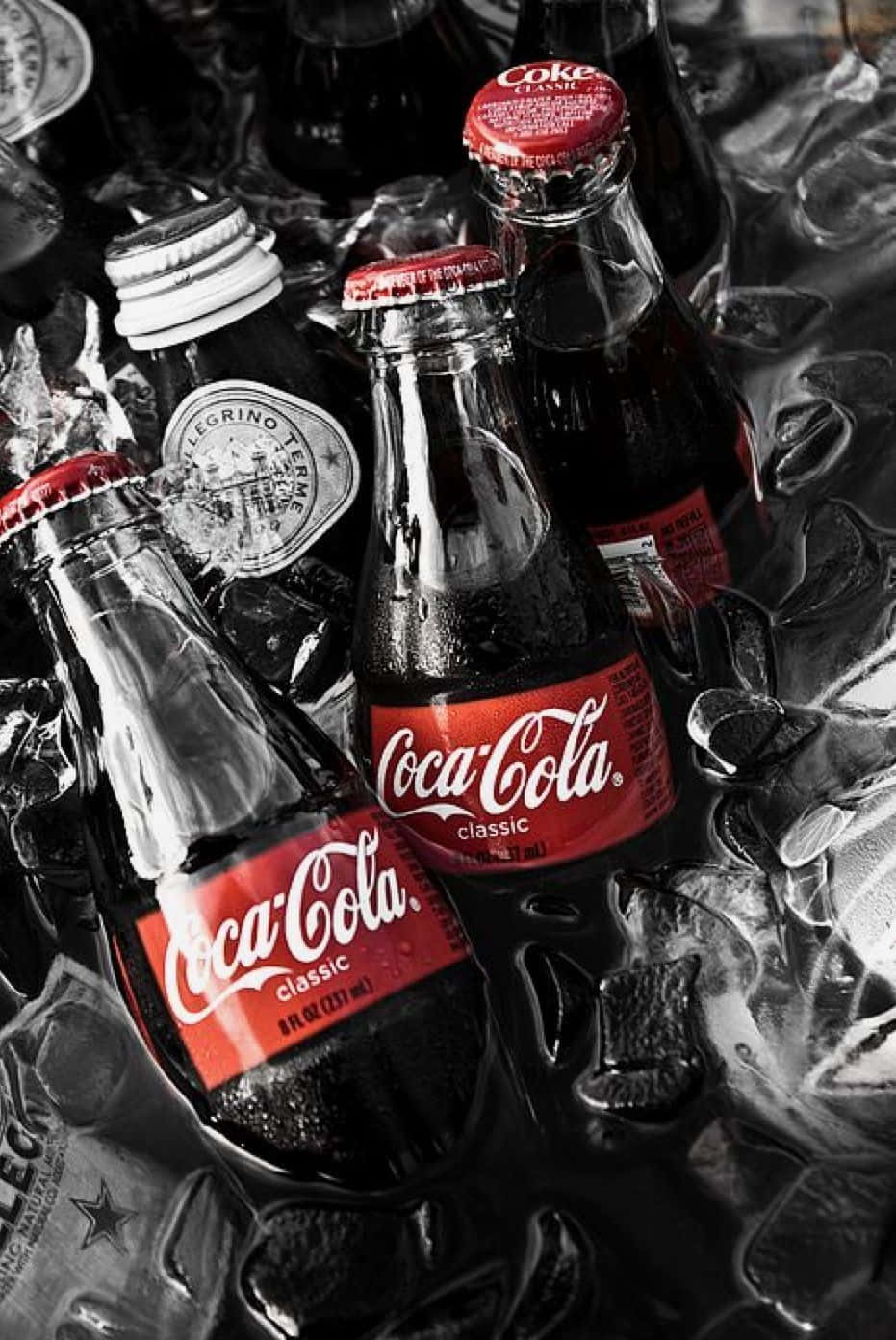 coca cola 桌布 壁紙 — 經典可口可樂瓶置於碎冰中，選擇性紅色突出標誌性品牌。