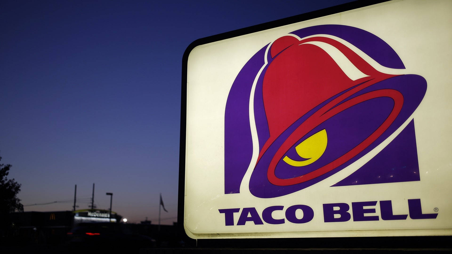 經典塔可鐘招牌 壁紙 — 一個明亮照明的Taco Bell招牌在暮色天空中發光，背景中可見麥當勞招牌。