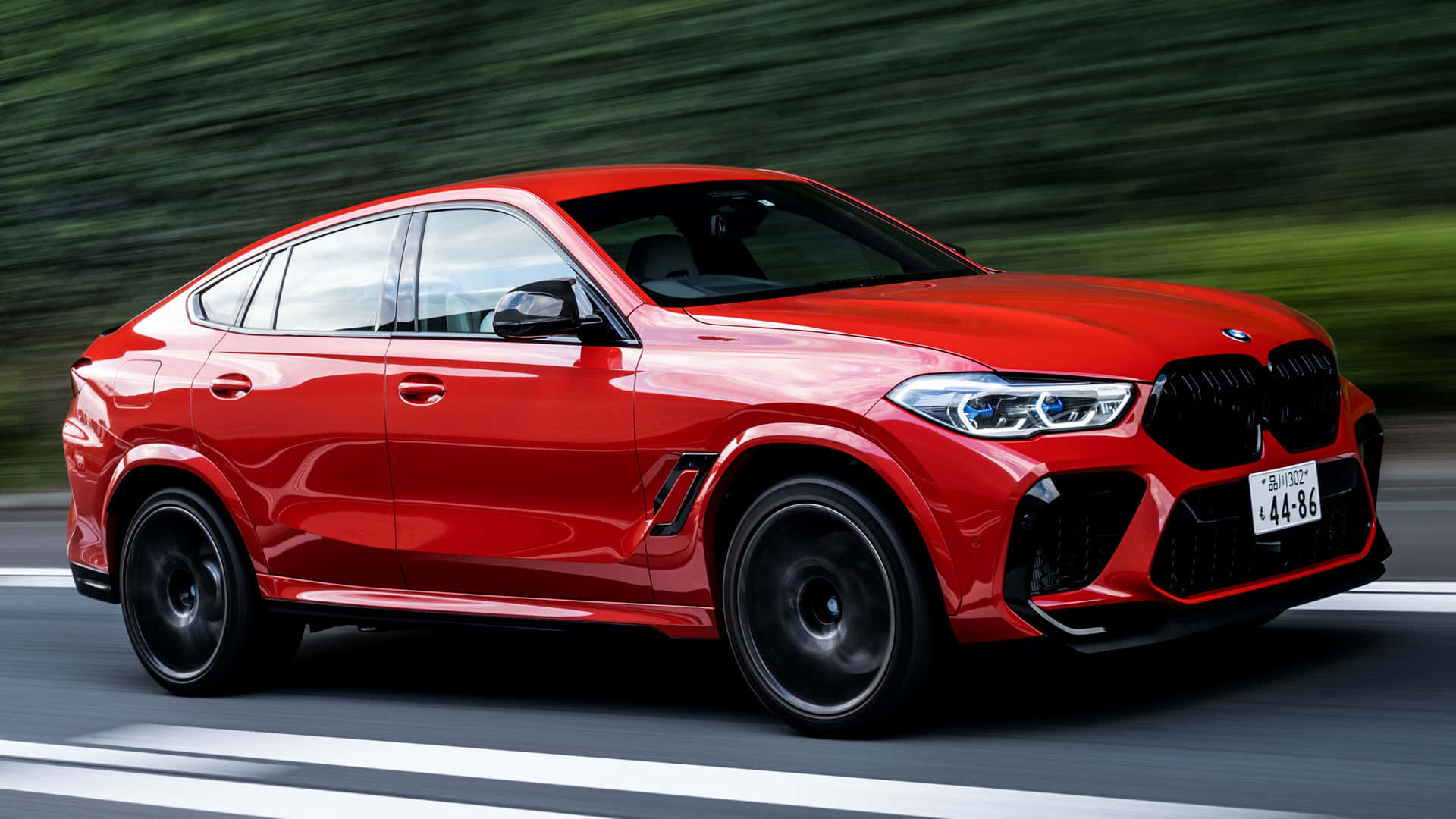 經典奢華 — BMW X6 M 壁紙 — 一輛鮮紅色的BMW X6 M在模糊的綠色背景中沿著道路疾馳。