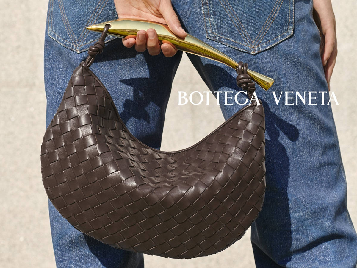 近距離拍攝一名手持Bottega Veneta編織皮革手袋（配有金色手柄）的人。