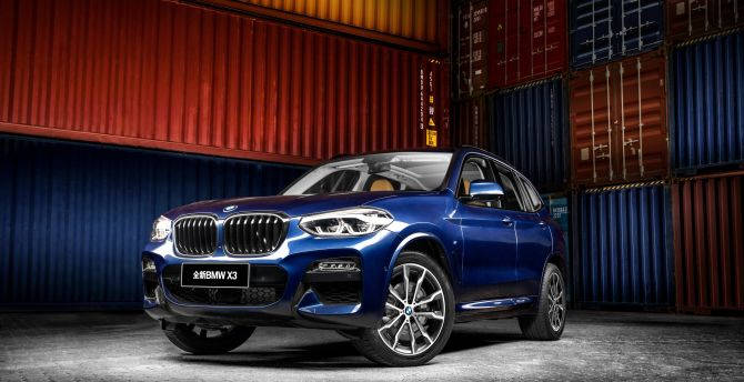 藍色BMW X3 SUV停在彩色貨運集裝箱前。
