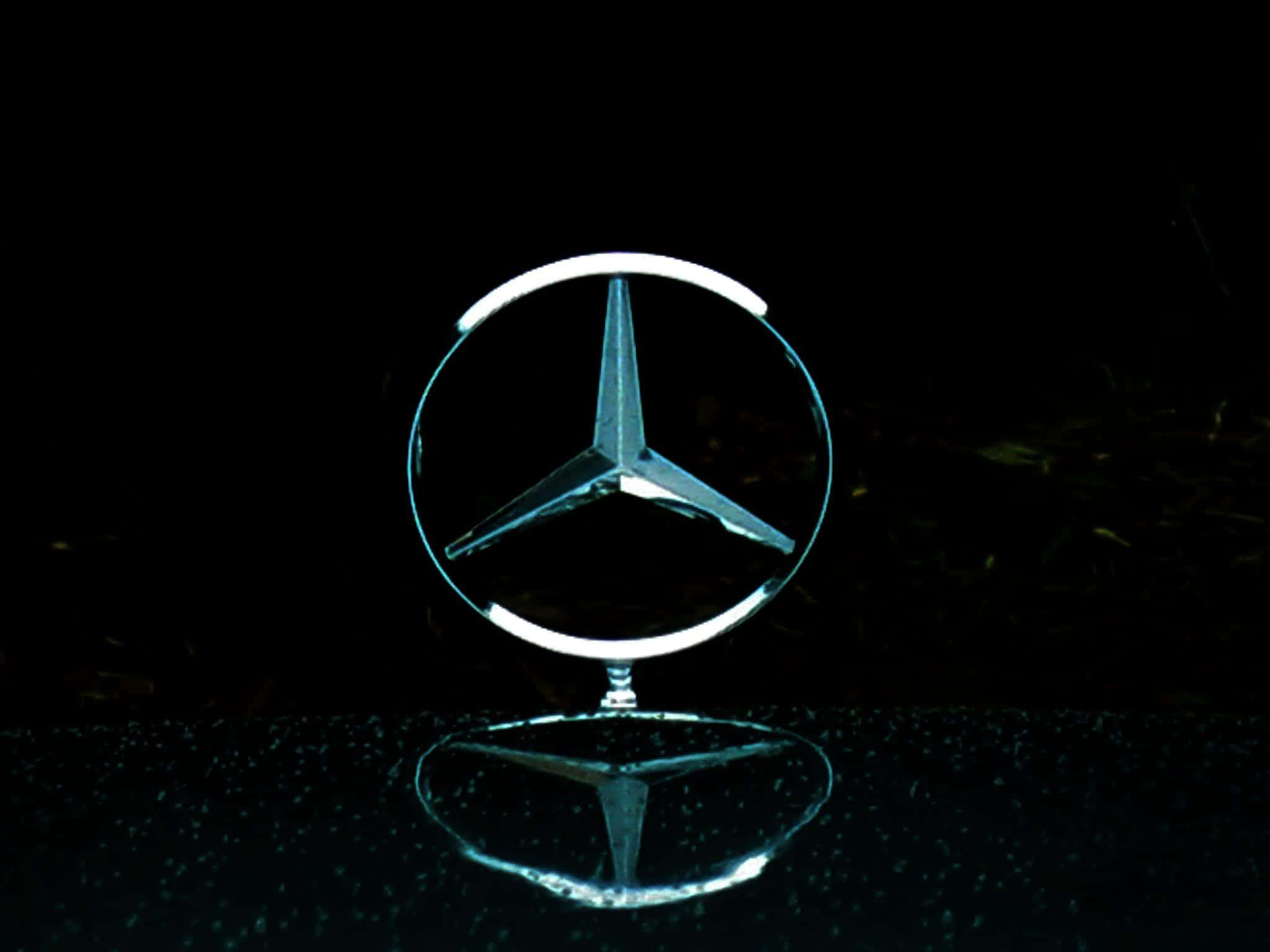 經典梅賽德斯-奔馳標誌 壁紙 — 一個發光的 Mercedes-Benz 標誌置中於反射表面上，背景為純黑色。