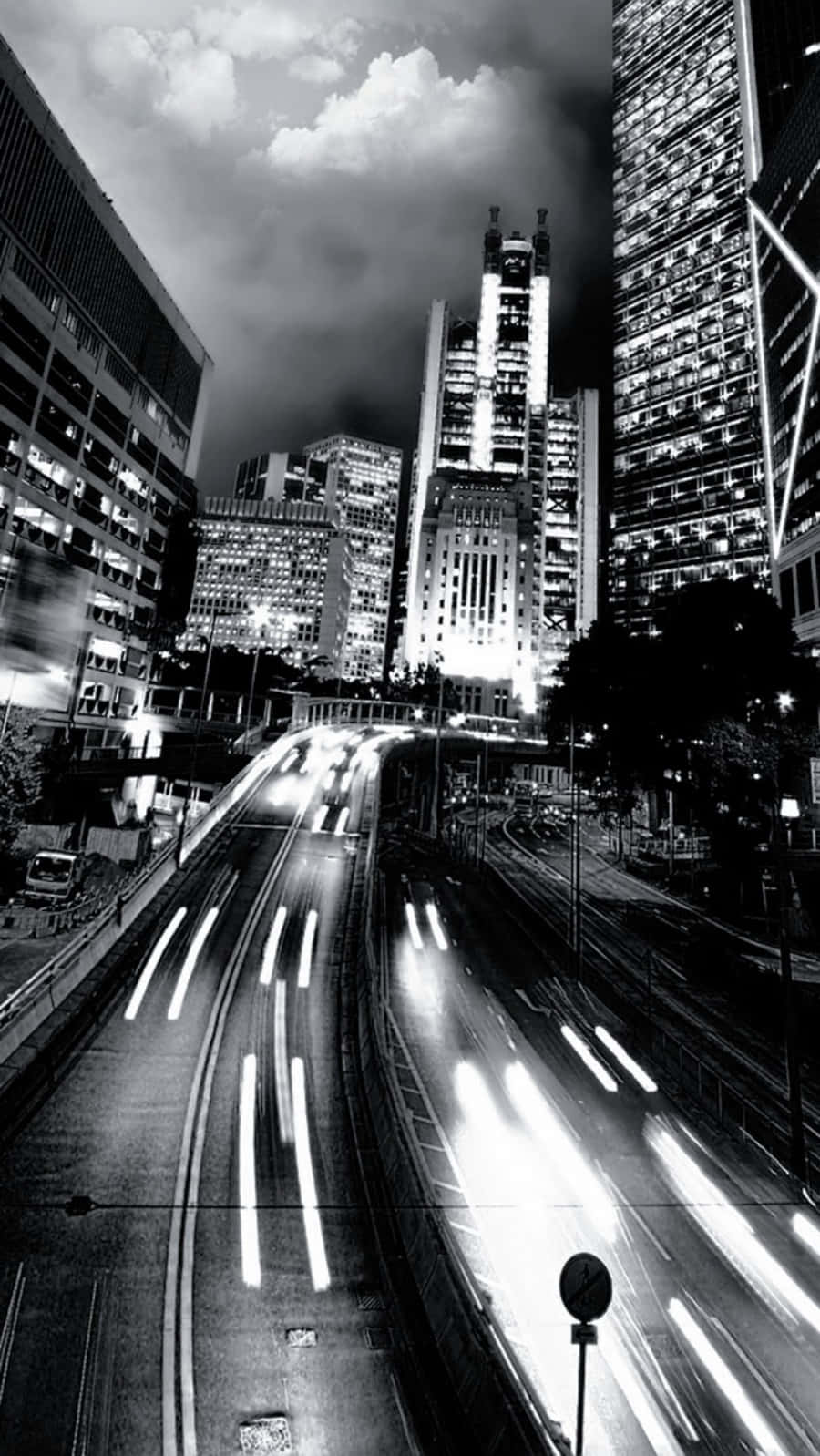 經典極簡黑白 iPhone 壁紙 — 高對比度的黑白城市夜景，車流燈光在高聳摩天大樓下流動形成光軌。