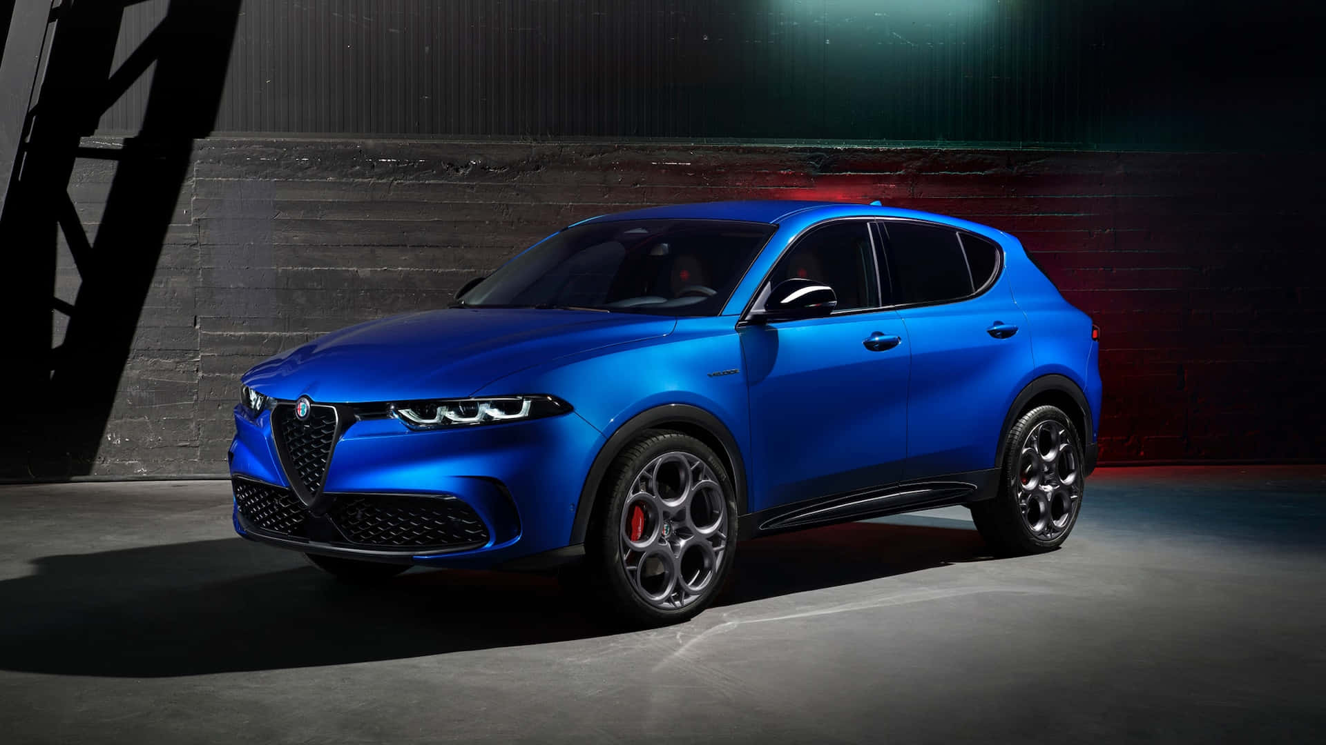 經典歐洲賽車優雅 壁紙 — 一輛充滿活力的藍色 Alfa Romeo SUV 在戲劇性的攝影棚燈光下，在深色紋理牆壁前閃閃發光。