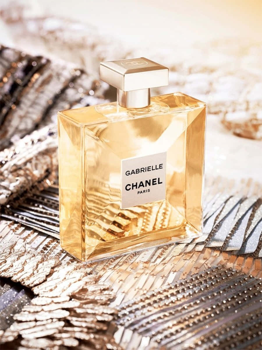 經典永恆——香奈兒標誌 壁紙 — 金色 Chanel Gabrielle 香水瓶在溫暖燈光下閃耀於閃爍的金屬布料表面。