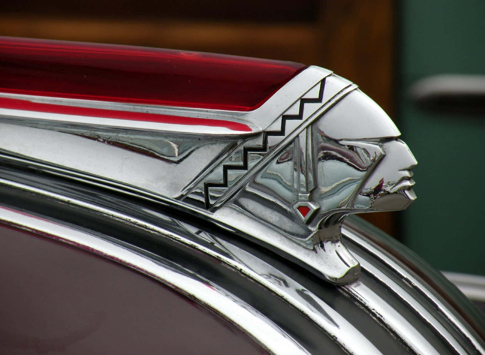 Car Hood 桌布 壁紙 — 經典汽車鍍鉻引擎蓋飾件的特寫，造型為風格化的美洲原住民酋長，帶有紅色點綴。
