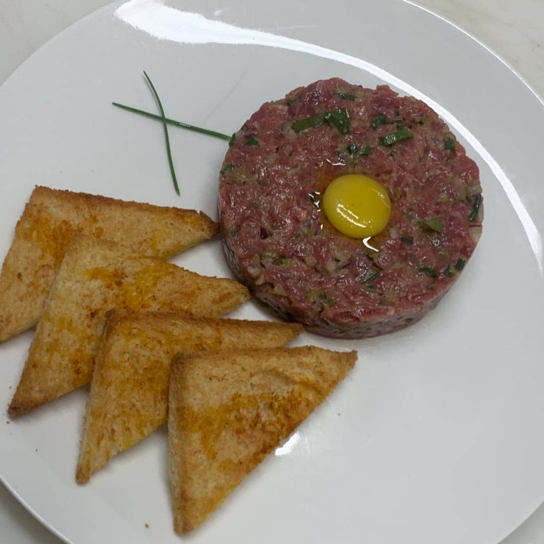 生牛肉他他配生蛋黃和細香蔥，伴以烤麵包三角形。