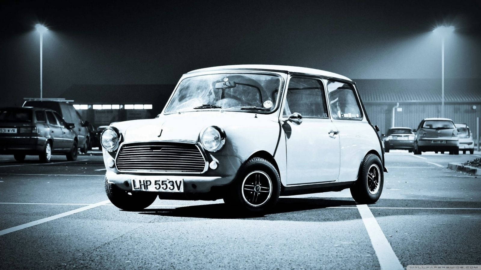 一輛白色經典Mini Cooper在夜間停車場停泊在街燈下。