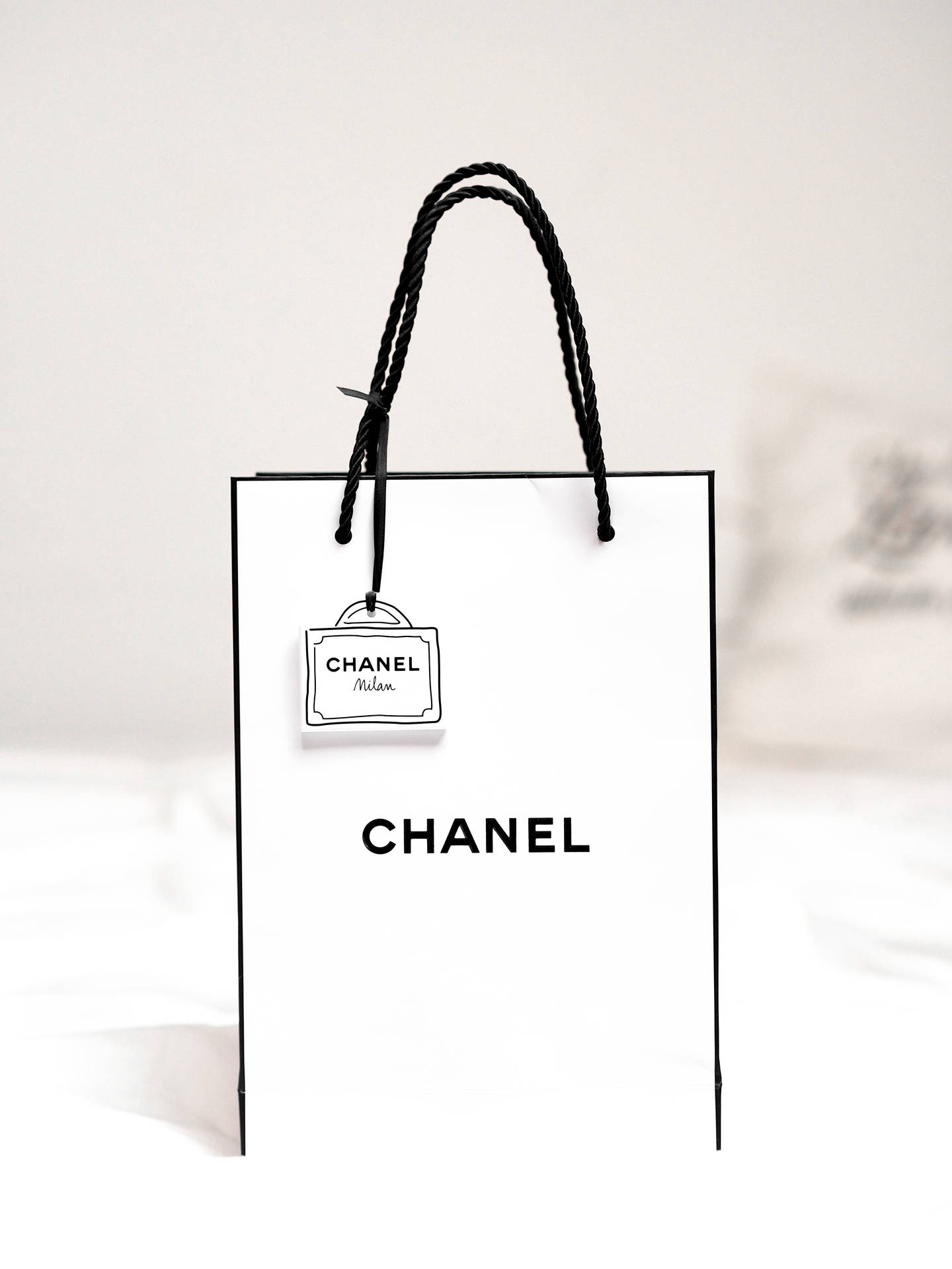 一個白色Chanel購物袋，帶有黑色手柄和標誌，置於柔和背景上。 — 路易威登 壁紙