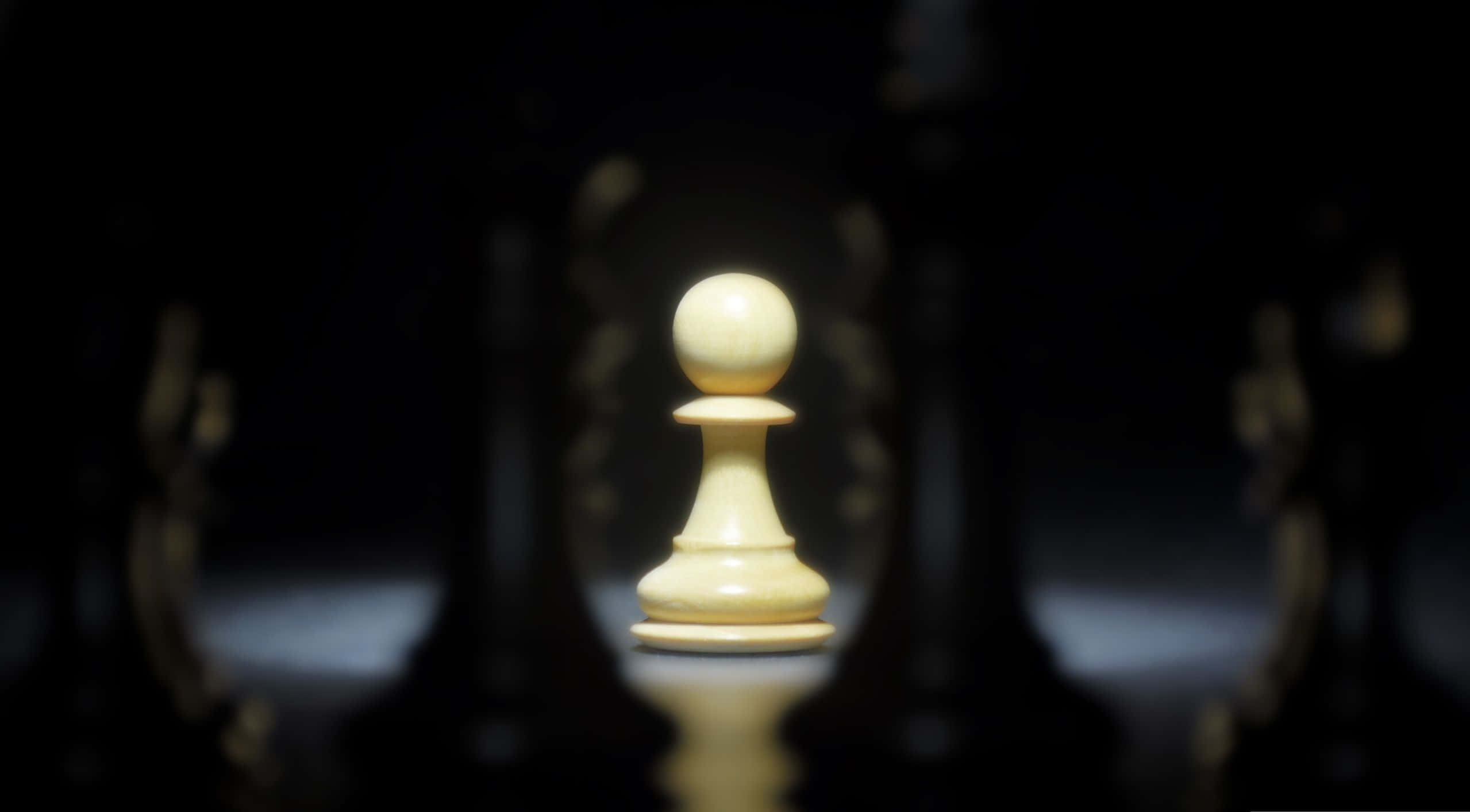 經典的象棋遊戲 壁紙 — 一個單獨照亮嘅白色象棋兵喺黑暗模糊嘅背景中，對住對面嘅黑色棋子，清晰對焦。