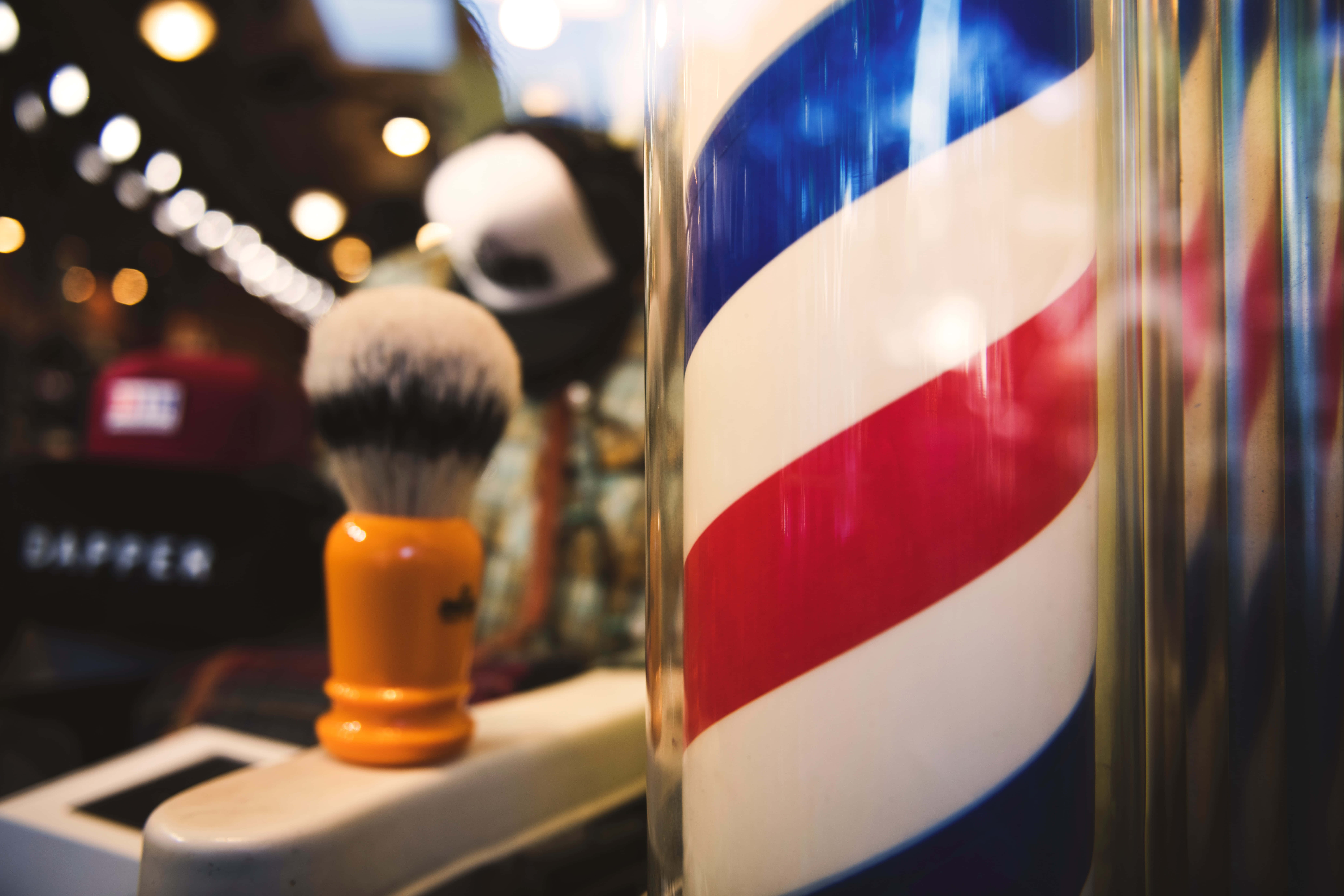 Barber 桌布 壁紙 — 經典紅白藍理髮柱旁邊放著橙色手柄的剃鬚刷，在溫暖燈光的理髮店內特寫。