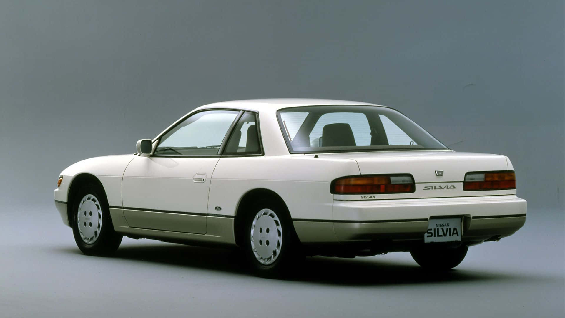白色日產Silvia轎跑車，攝影棚拍攝，從後方四分之三角度。