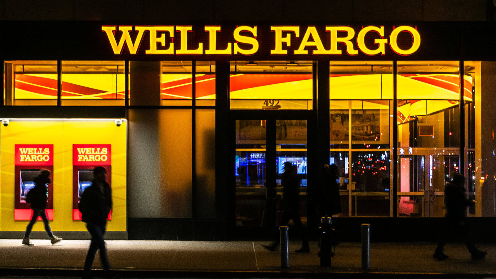 人們夜晚經過帶有黃色標誌的 Wells Fargo 銀行。