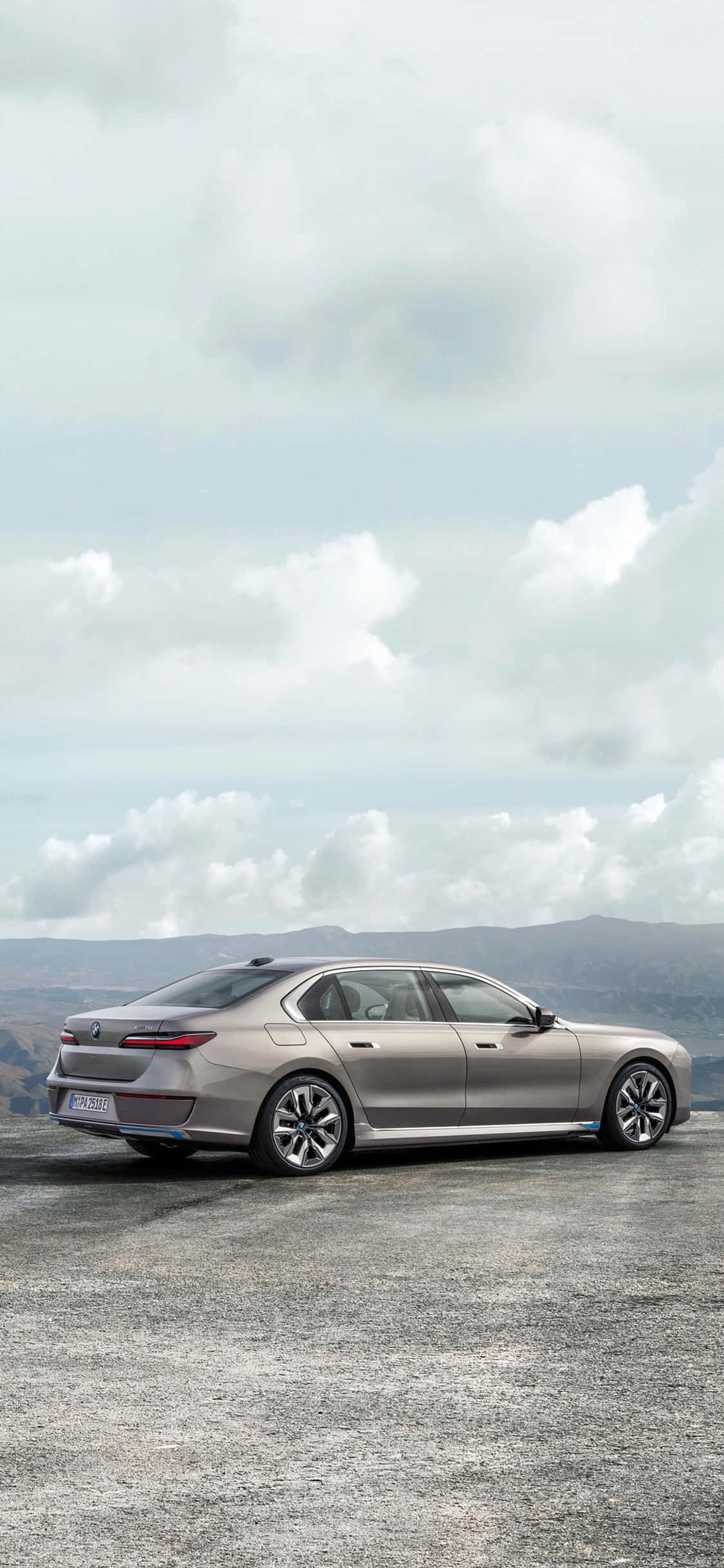經典組合——iPhone X 與 BMW 壁紙 — 一輛時尚的銀色轎車停泊在碎石觀景點，遠山在陰天之下。