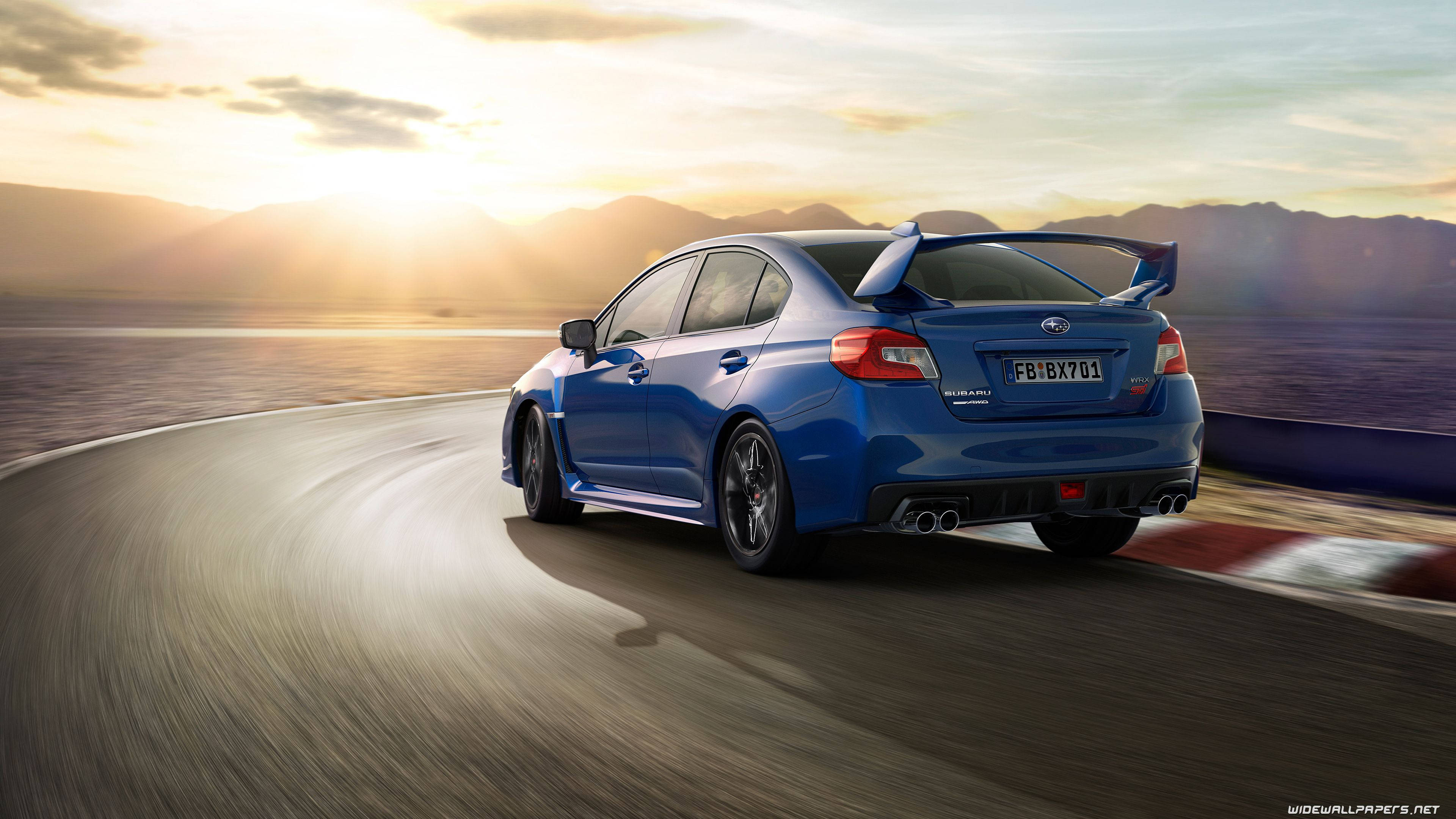 經典藍色斯巴魯Impreza風采盡顯 壁紙 — 一輛充滿活力的藍色Subaru WRX STI在日落時分沿著蜿蜒的海岸公路疾馳，背景是山脈。