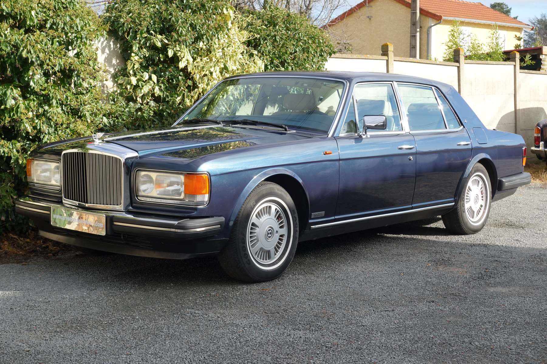 Bentley Eight 桌布 壁紙 — 經典藍色賓利房車在明亮日光下停泊在碎石上，旁邊有綠色灌木叢。