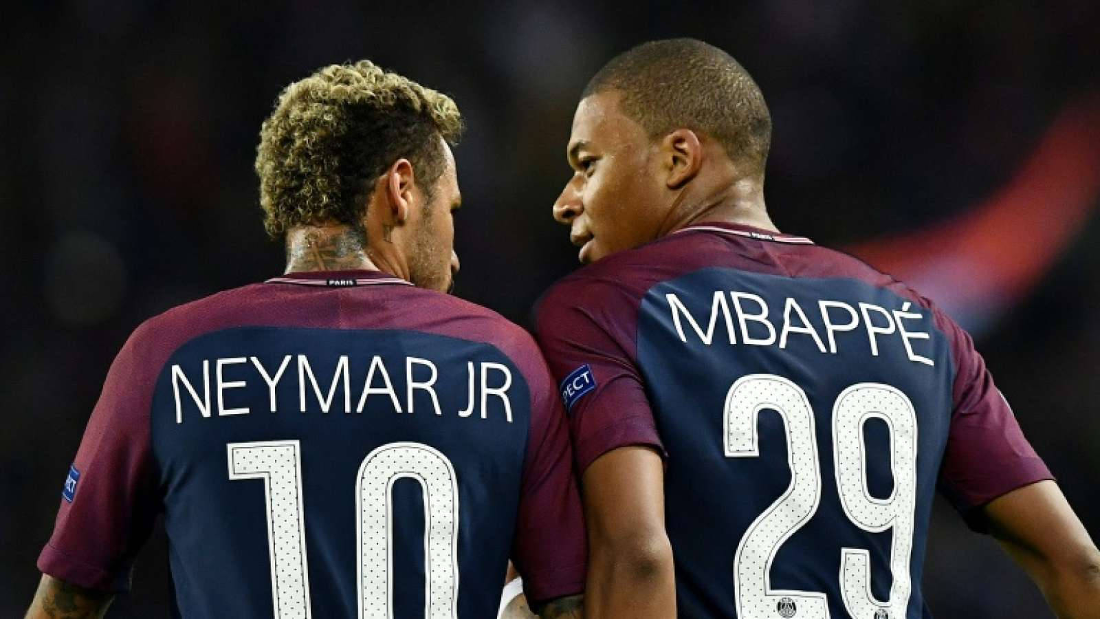 兩位足球員尼馬（Neymar Jr）和麥巴比（Mbappé）身穿栗紅色球衣，在燈光昏暗的球場上專注交談。