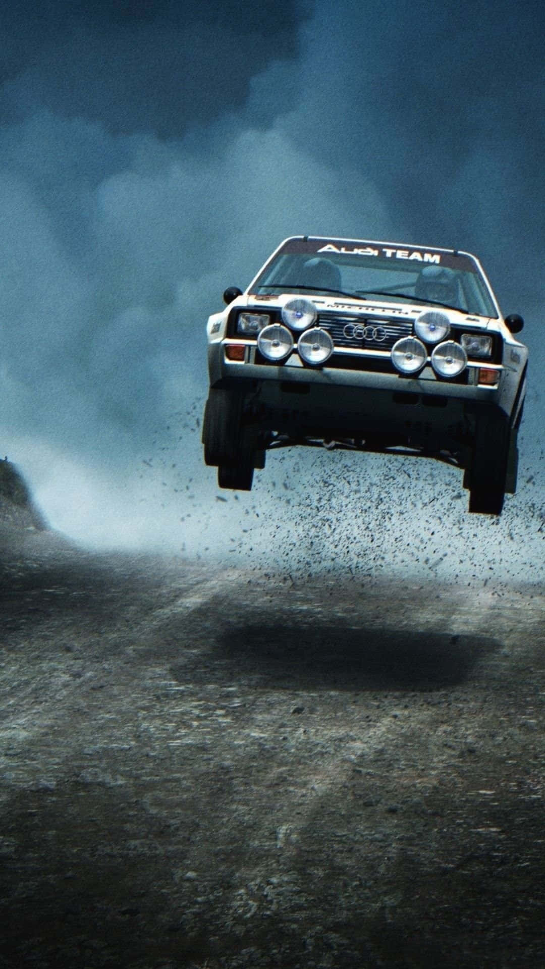 經典賽車飛躍 —— Dirt Rally 遊戲 iPhone 壁紙 — 一輛白色奧迪拉力賽車在泥濘賽道上空飛馳，上方有黑暗的暴風雲。