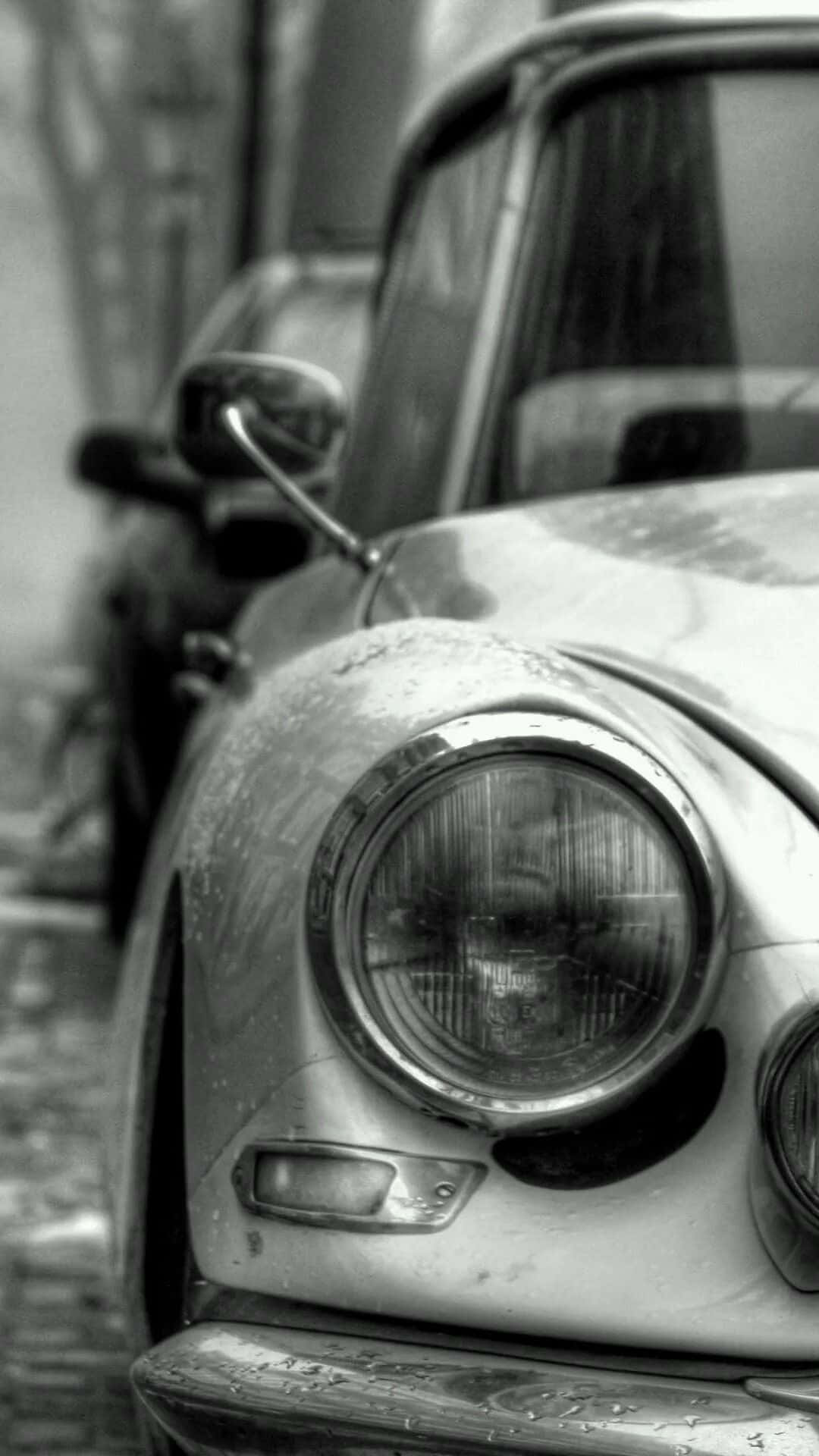 經典車頭燈特寫 iPhone 壁紙 — 經典車風化前端的黑白特寫，圓形頭燈和引擎蓋上的雨滴。