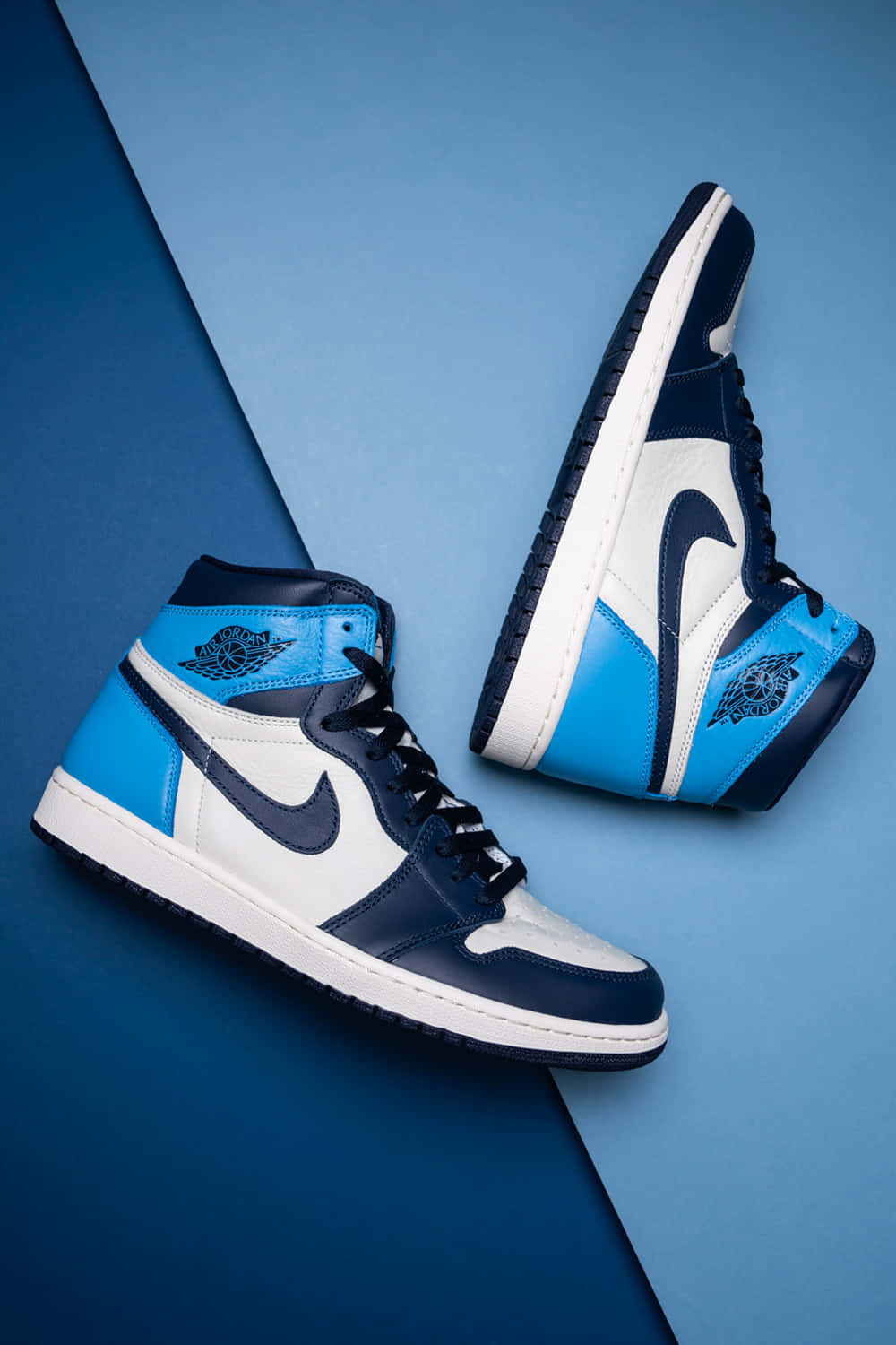 經典造型搭配現代風味 - Nike Air Jordan 壁紙 — 一對藍、白、黑色高筒運動鞋，傾斜放置在分割的藍色背景上。