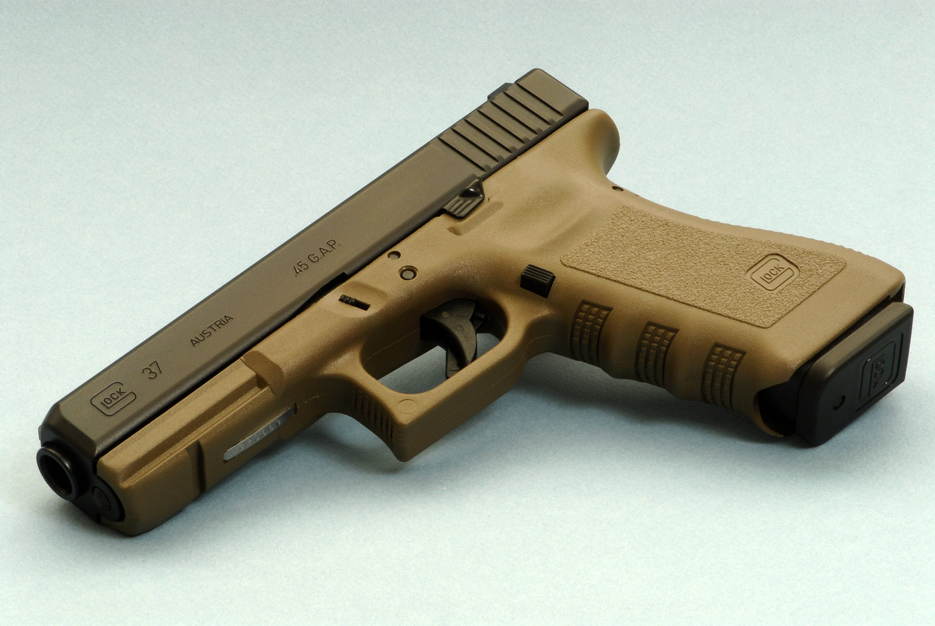 經典銅色 Glock 37 壁紙 — 一支棕褐色和黑色的Glock 37手槍，帶有.45 GAP口徑標記，斜放在純淺灰色表面上。