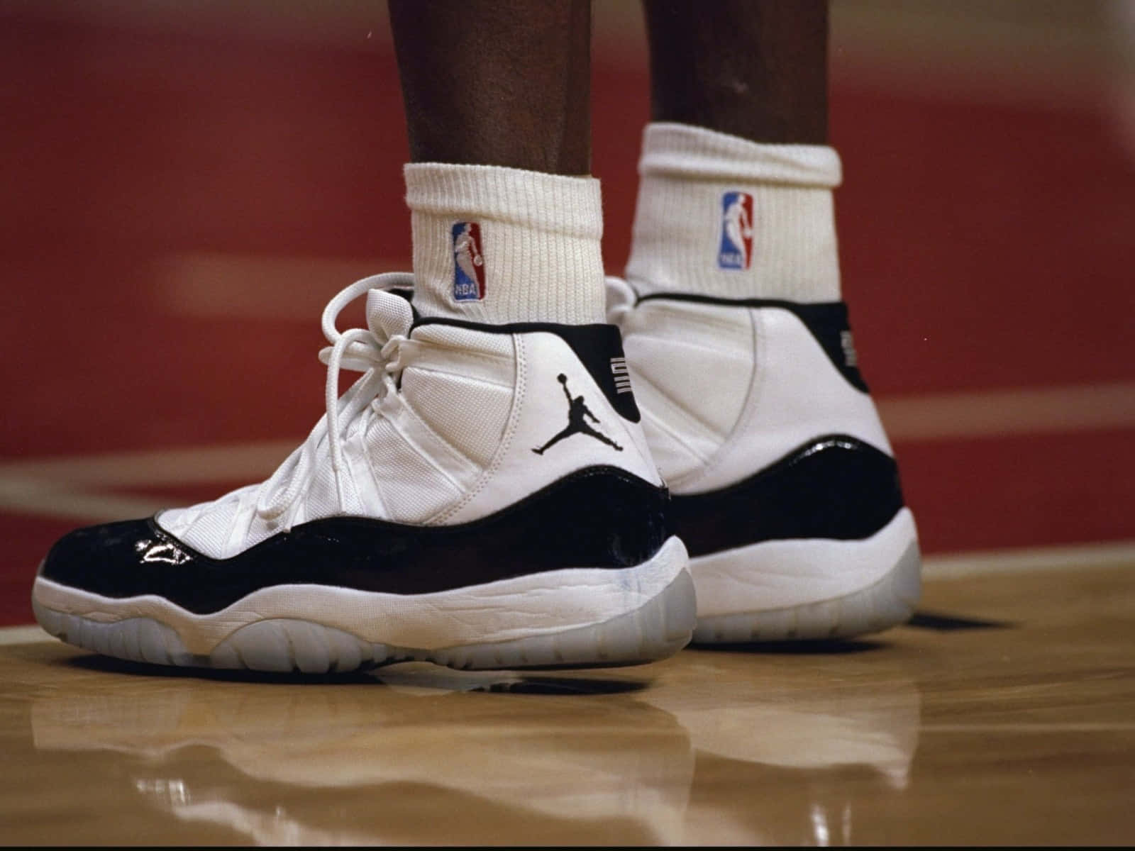 佐敦 桌布 壁紙 — 經典黑白 Air Jordan 11 運動鞋在拋光籃球場上的特寫，搭配NBA襪子。