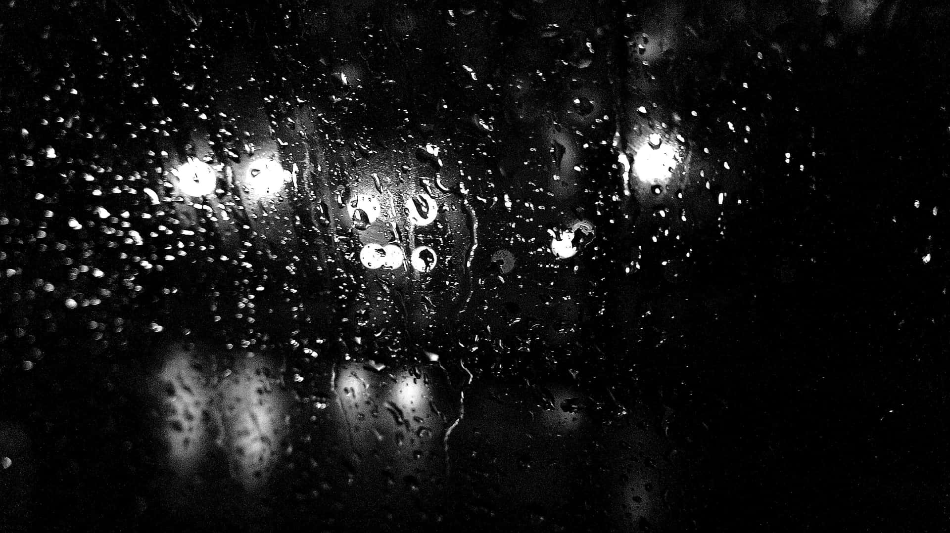 窗戶上的雨滴在夜間反射城市燈光，黑白效果。