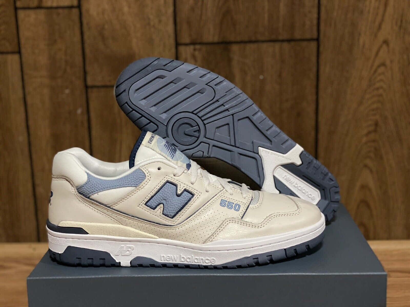 米色和海軍藍色的New Balance 550運動鞋放在鞋盒上，鞋底翹起。