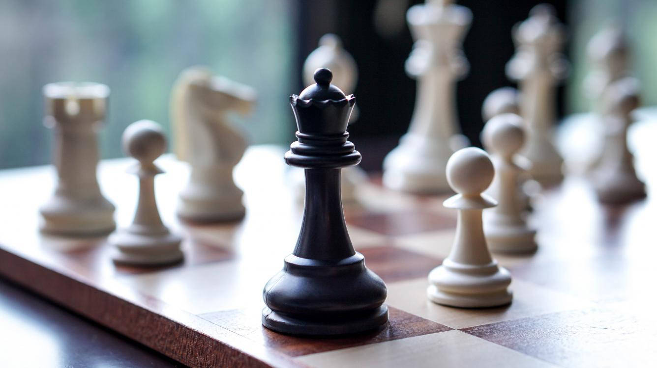 經典黑皇后棋子：權威與智慧的象徵 壁紙 — 黑色國際象棋國王特寫，高高矗立在木製棋盤上，背景有模糊的白色棋子。