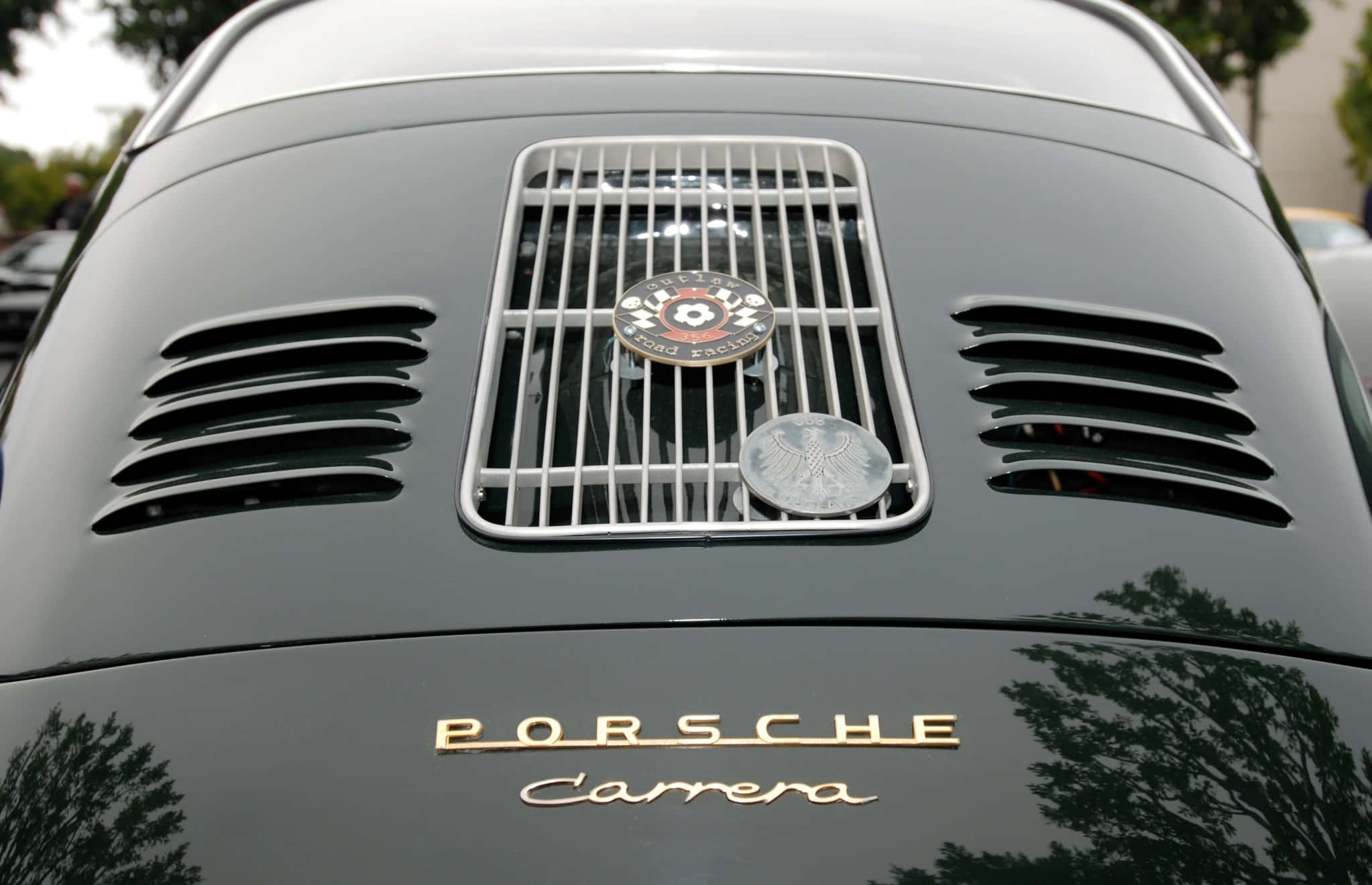 Car Grill 桌布 壁紙 — 經典黑色保時捷Carrera引擎蓋特寫，帶有鍍鉻格柵和徽章，反射樹木。