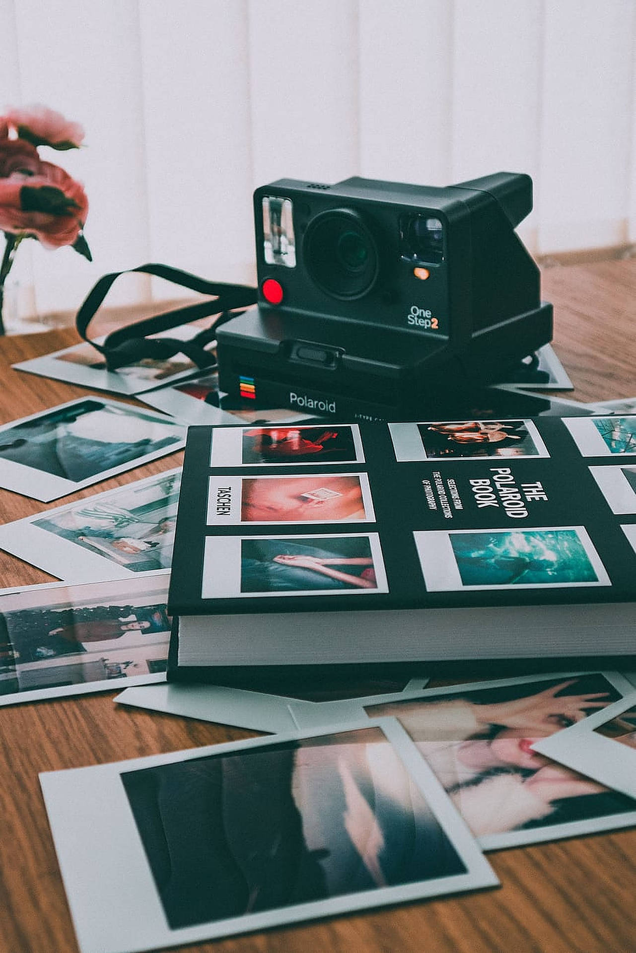 木桌上的復古Polaroid相機和即影即有照片，配有一朵粉紅花。