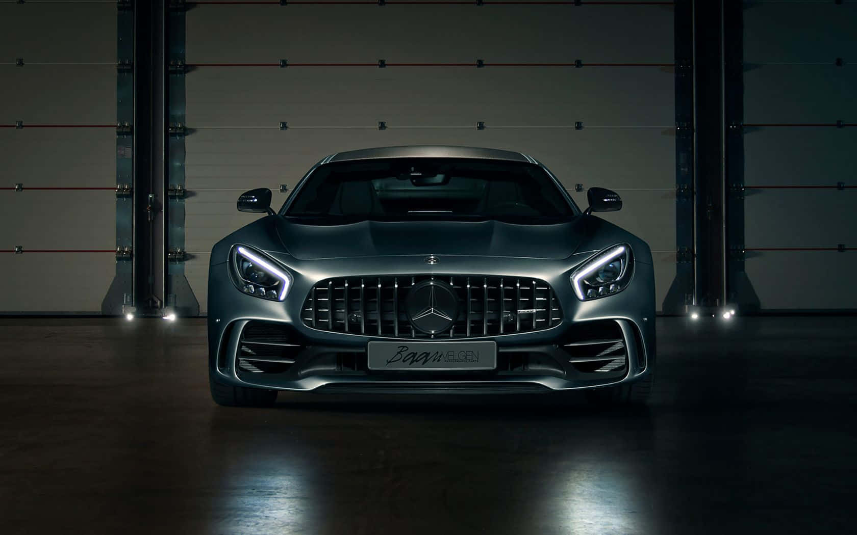 一輛啞光灰色 Mercedes-AMG GT 跑車在黑暗的工業車庫中被聚光燈照亮。