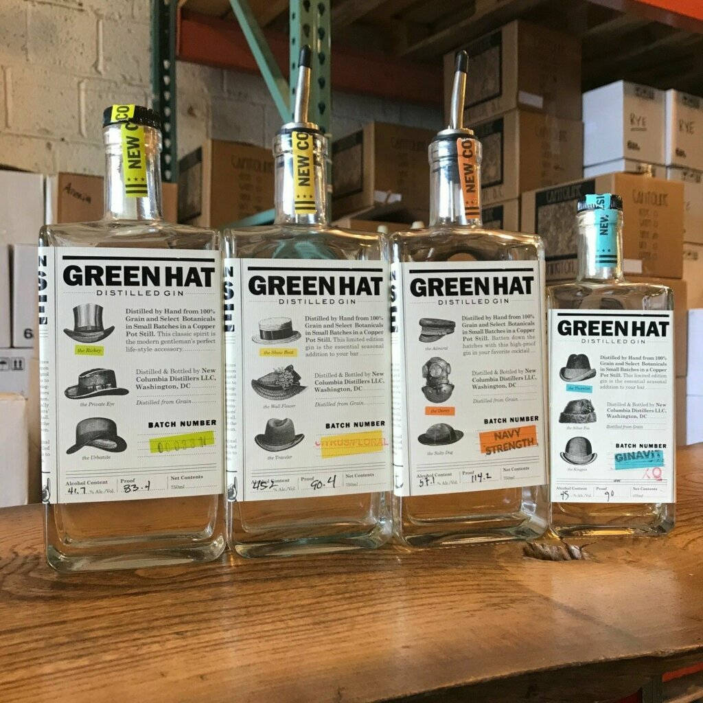 四瓶Green Hat Distilled Gin，帶有帽子主題標籤，喺倉庫嘅木架上。