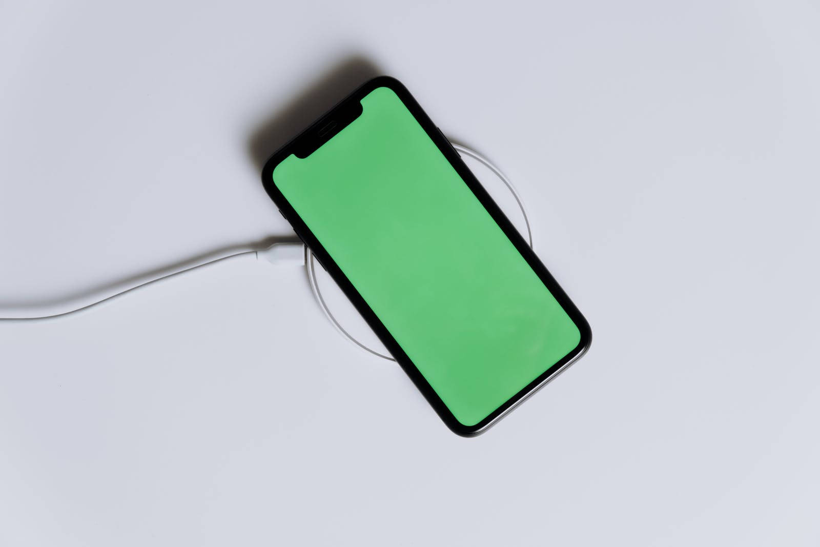 黑色智能手機在白色無線充電板上充電，綠色屏幕