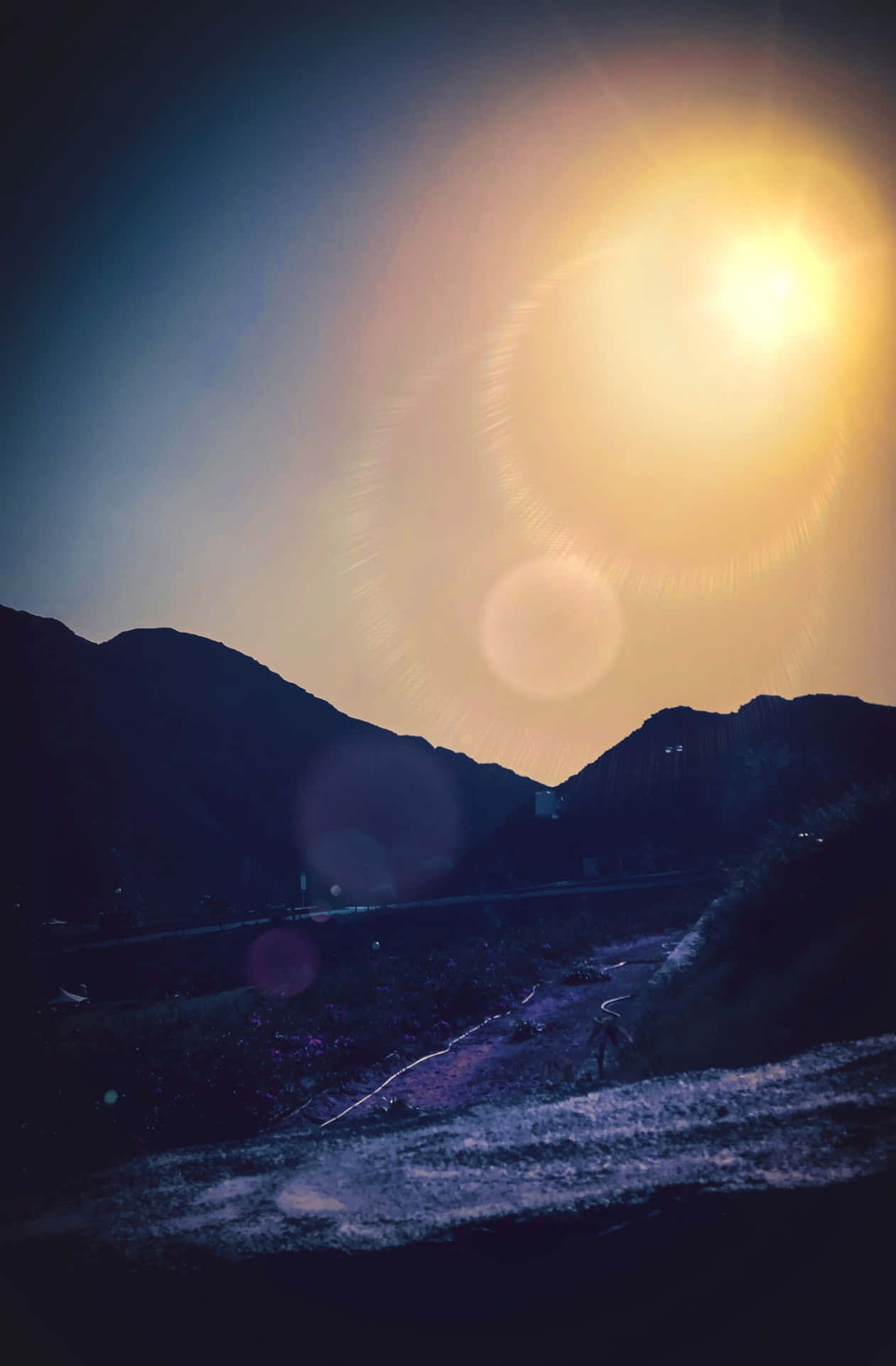 一個人在山路上行走，太陽在山峰後落下，伴隨著鏡頭光暈。