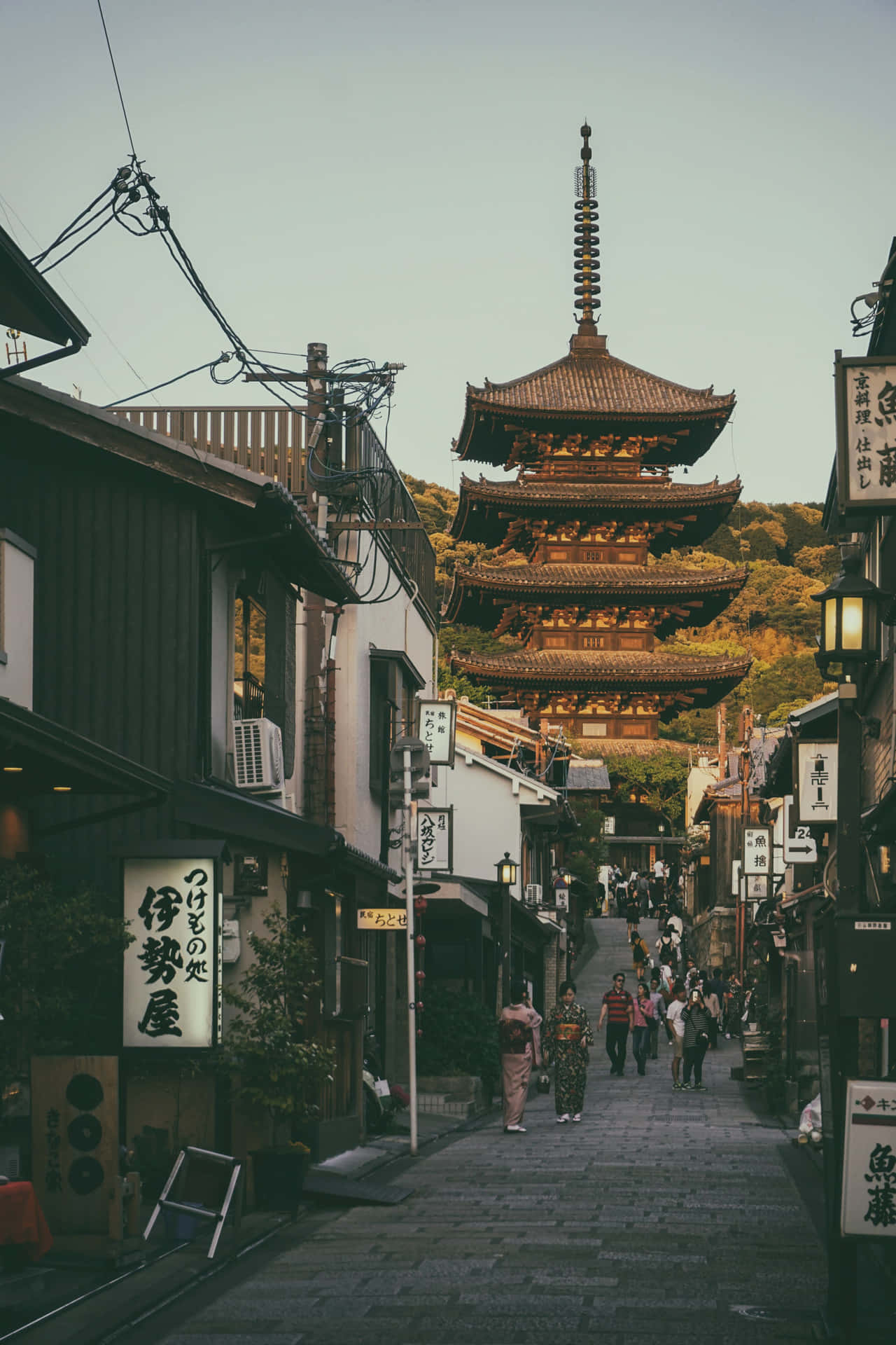 綠意盎然的鄉村風光，遠眺日本稲羽山 壁紙 — 京都一條狹窄的石板路，兩旁是傳統木造建築，向上通往一座沐浴在溫暖夕陽中的高聳寶塔。