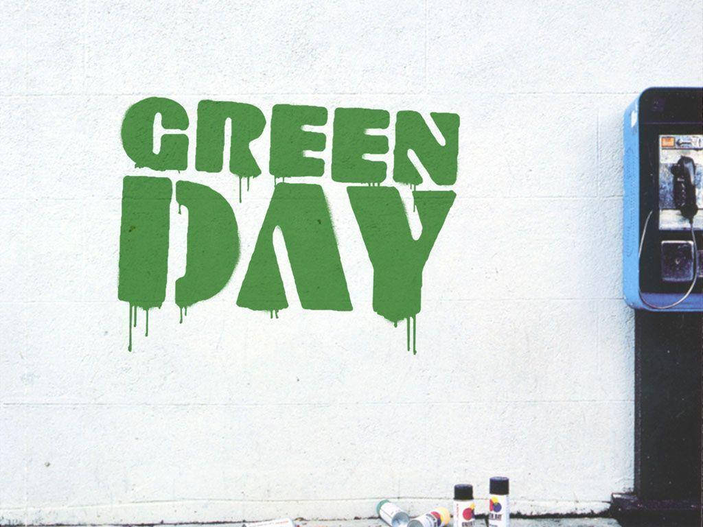綠日樂隊名稱塗鴉 壁紙 — 大膽的綠色塗鴉拼寫GREEN DAY，滴落在白色混凝土牆上，旁邊有一個藍色公用電話和噴漆罐。