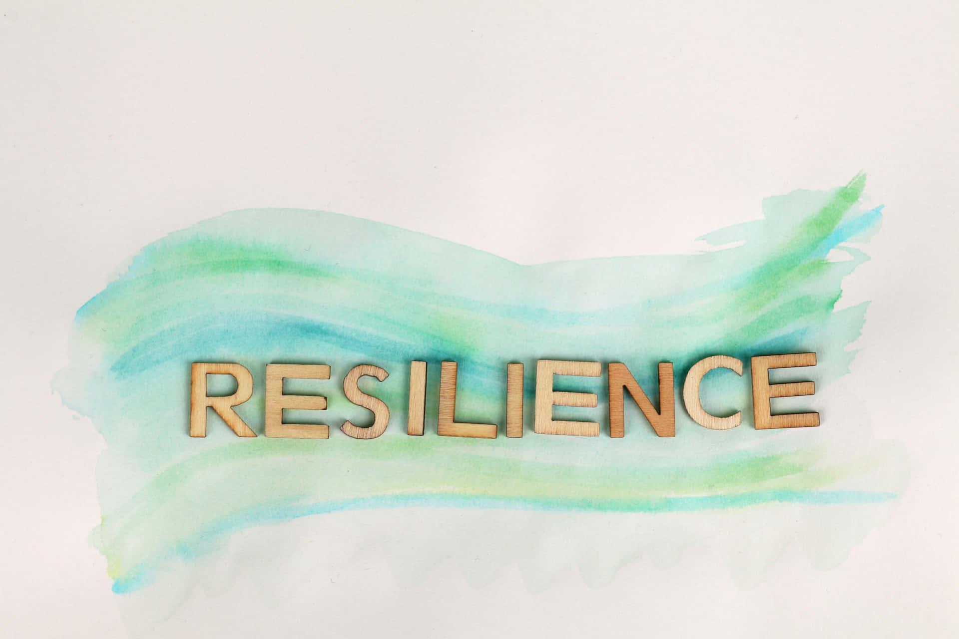 木製字母喺青綠色同薄荷綠色水彩背景上拼出「resilience」。