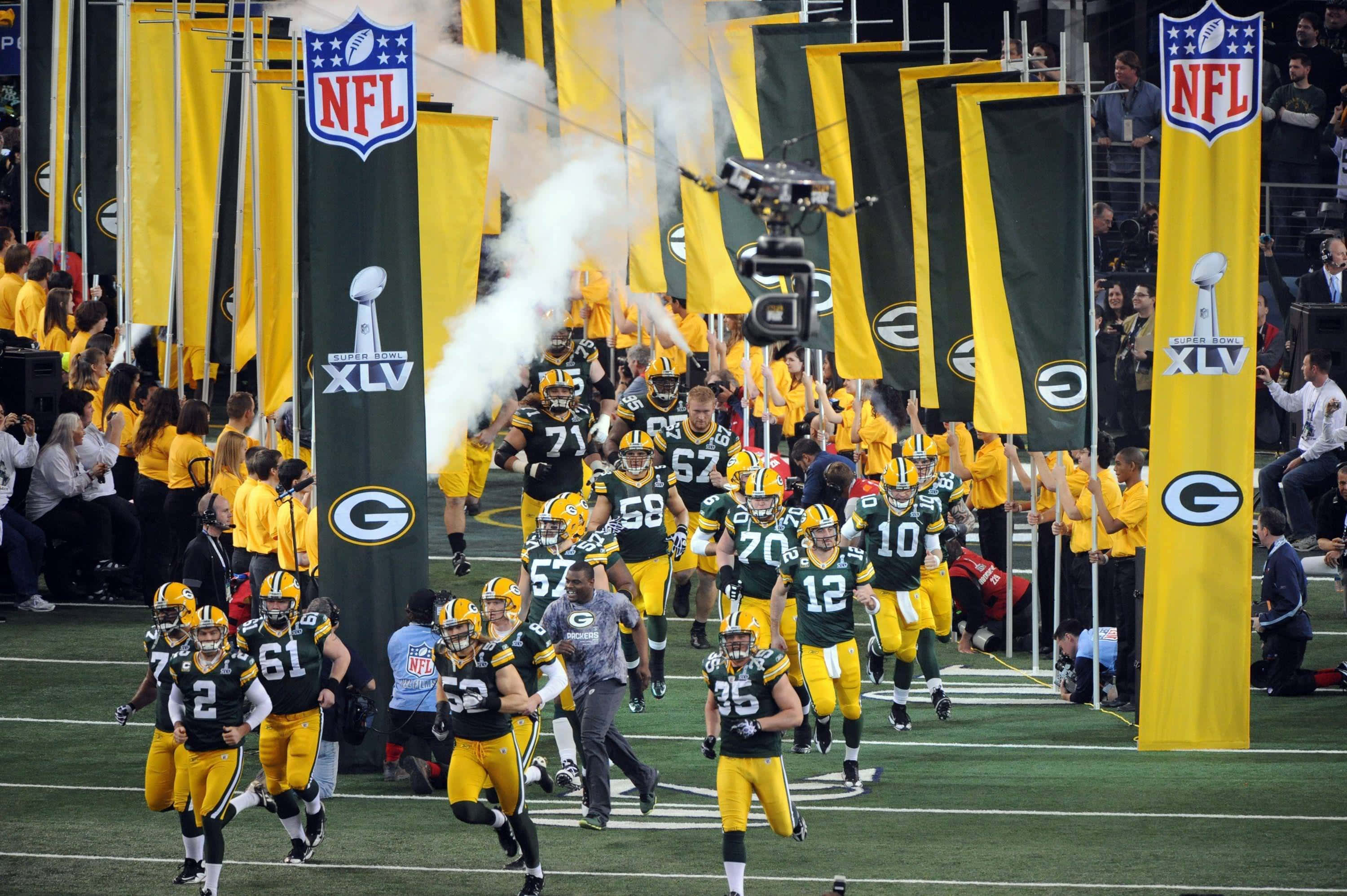 Packers 桌布 壁紙 — 綠灣包裝工美式足球員身穿綠色和金色球衣，穿過煙霧隧道跑入球場，兩旁有球隊旗幟和歡呼的球迷。