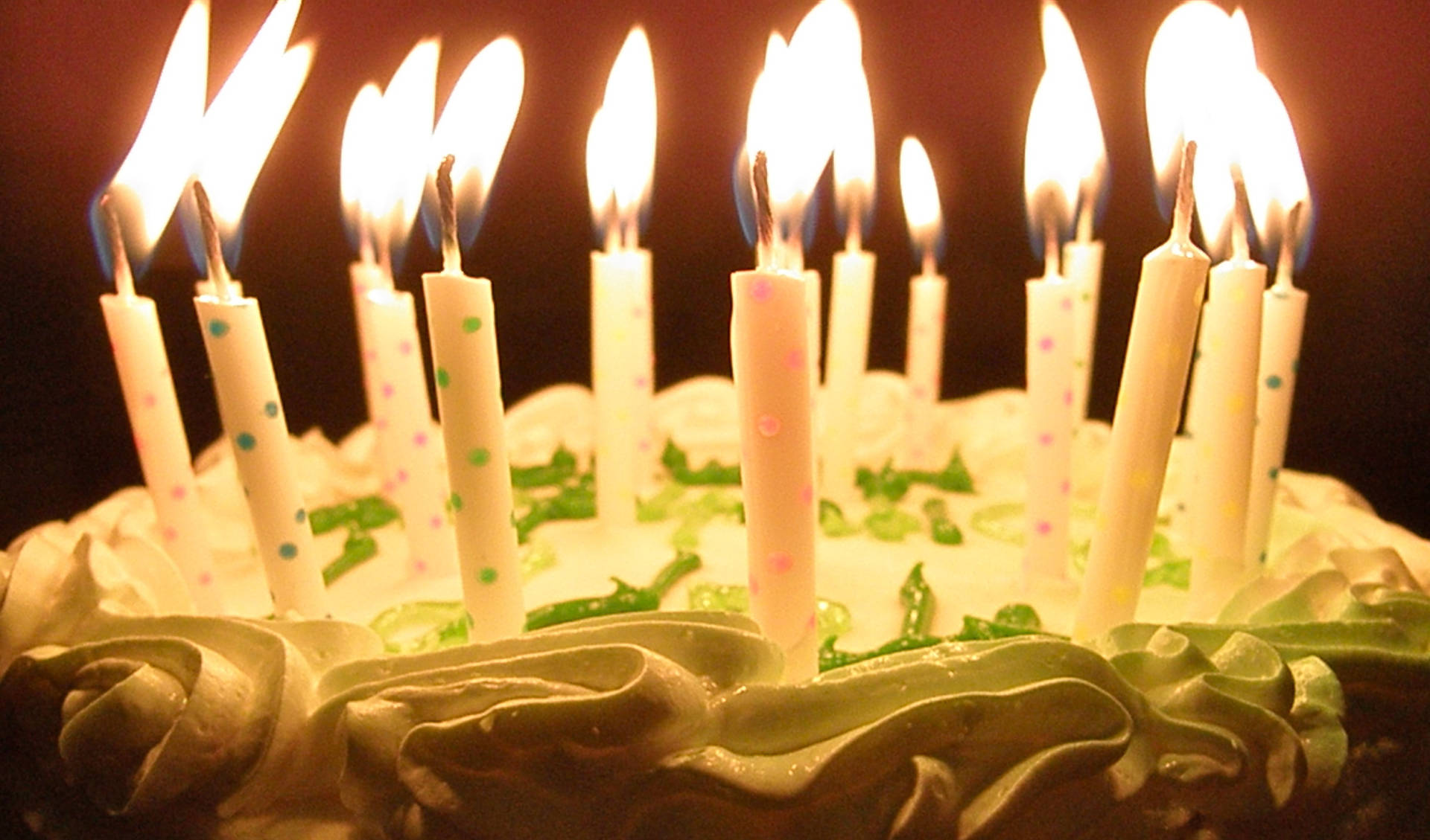 綠白生日蛋糕與蠟燭 壁紙 — 生日蛋糕特寫，蠟燭點燃，在黑暗背景下投射出溫暖的光芒。