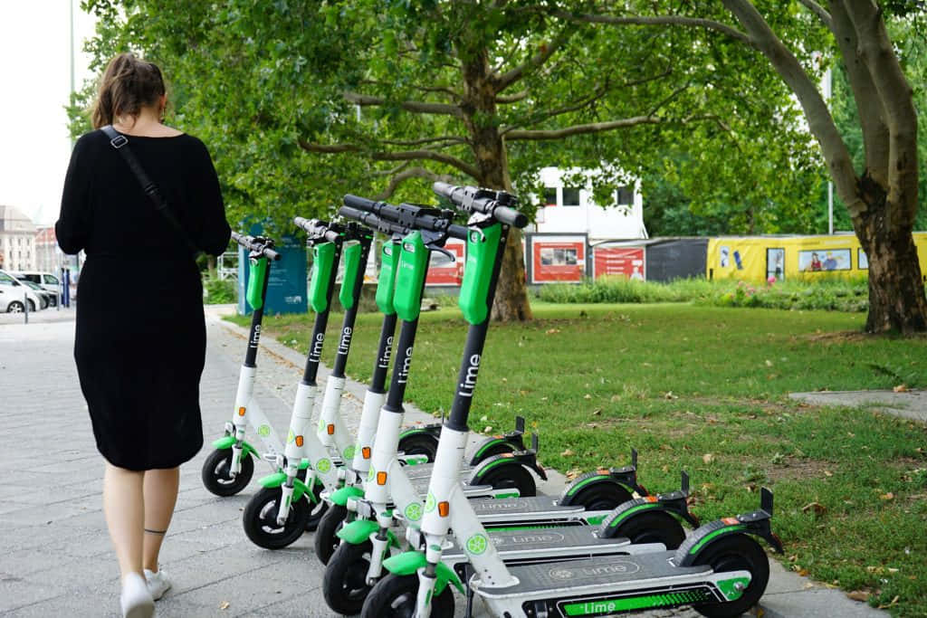 女子走過停放在城市人行道上的Lime電動滑板車。