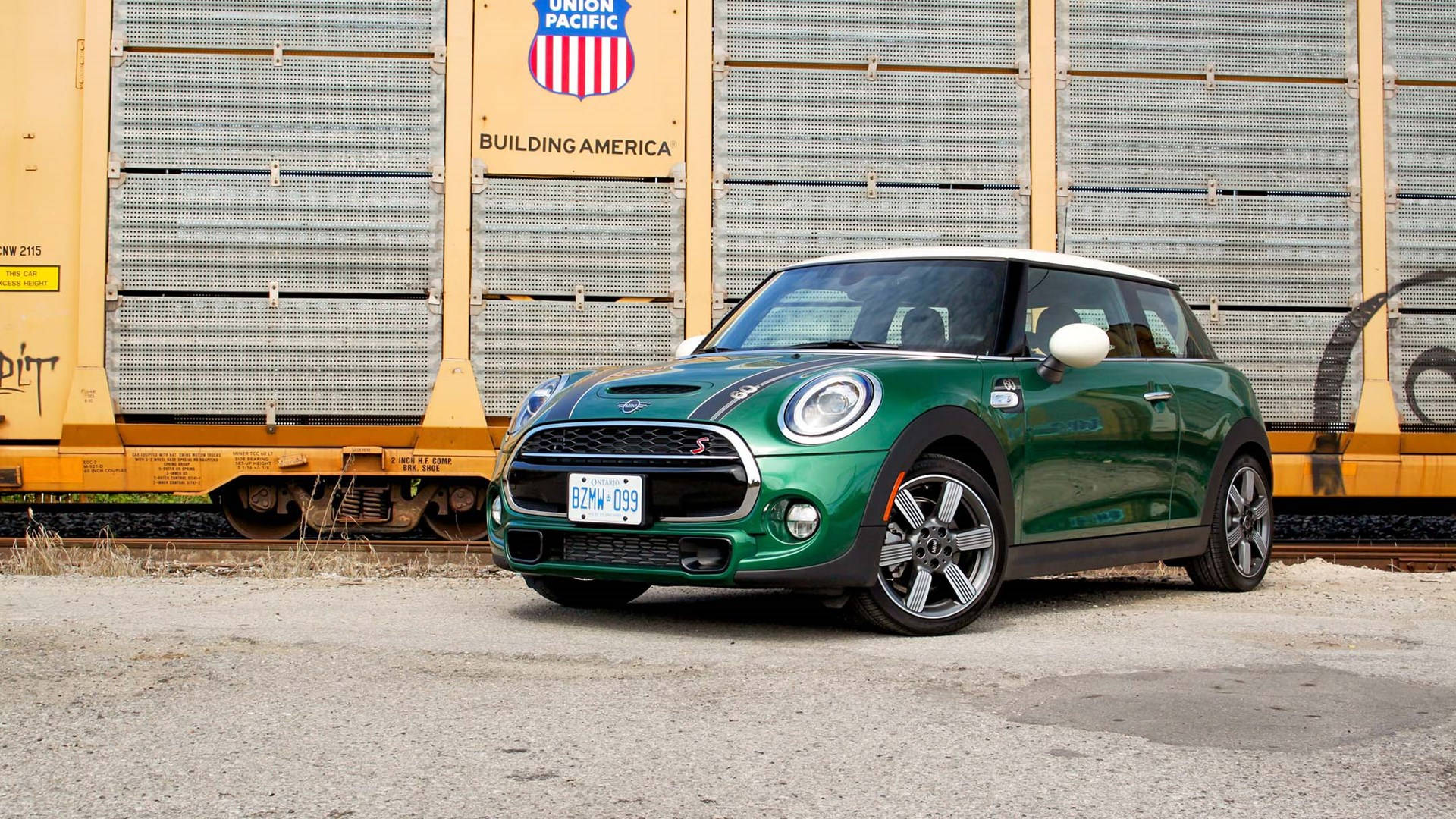 綠色Mini車停泊於金屬建築外 壁紙 — 一輛充滿活力的綠色MINI Cooper S停泊在碎石上，旁邊是一輛黃色的聯合太平洋貨運火車車廂。