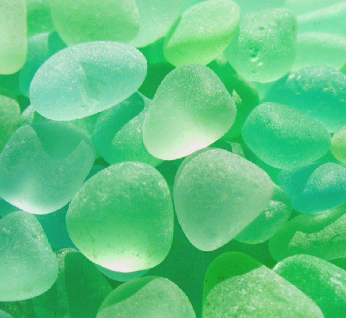沙灘上光滑綠色海玻璃卵石的特寫。