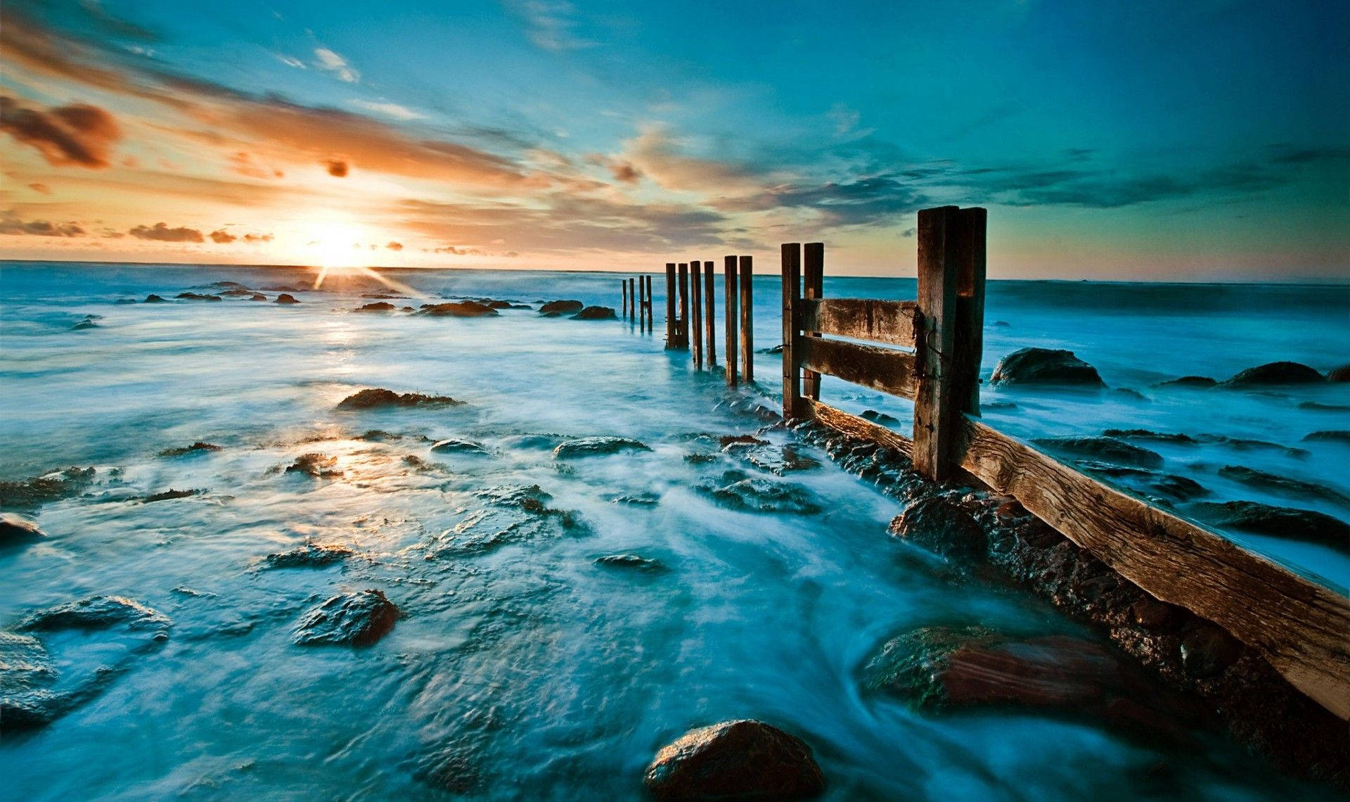 海洋上的夕陽，有木樁和水 — 綠色天空 壁紙