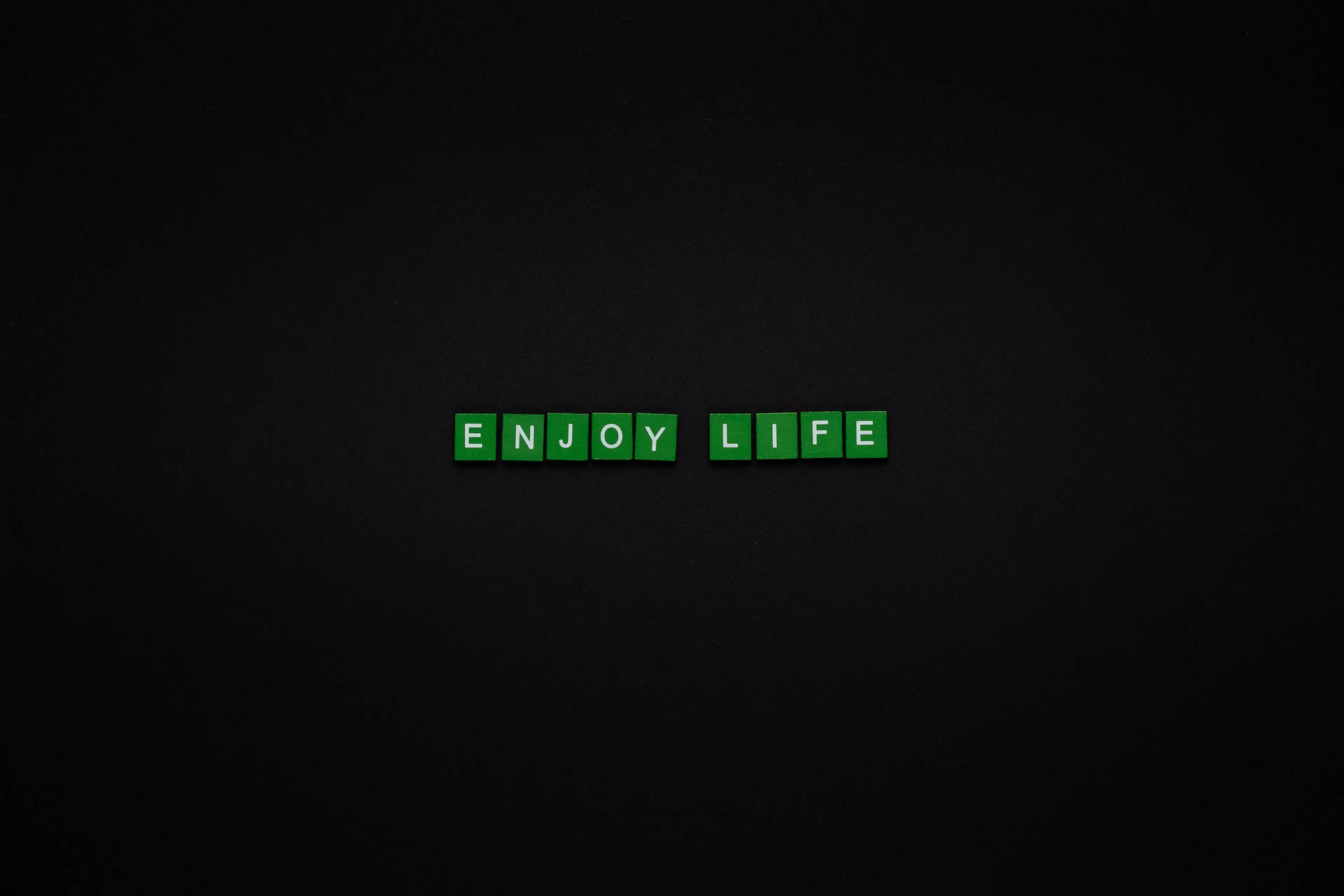 黑色動態圖 桌布 壁紙 — 綠色字母瓷磚在深色紋理背景中央拼出enjoy life。