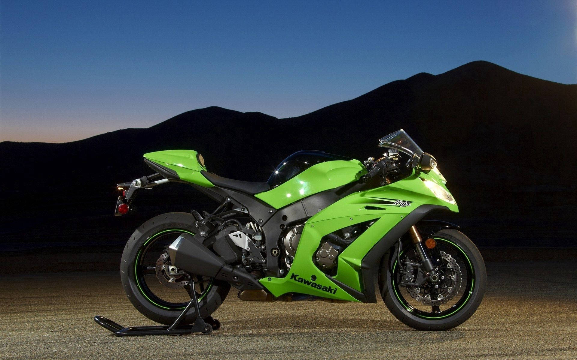黃昏時停在碎石上的綠色Kawasaki運動電單車，背後有山。