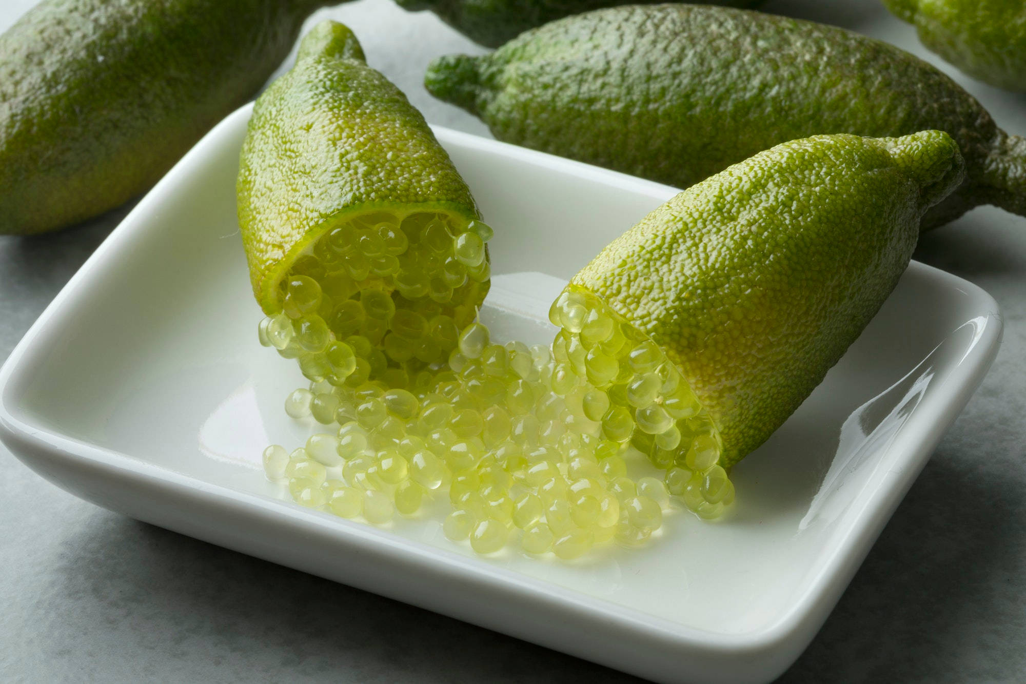綠色指 lime 果切開特寫 壁紙 — 新鮮金桔切開，露出閃閃發光的半透明種子，灑落在白色陶瓷碟上。