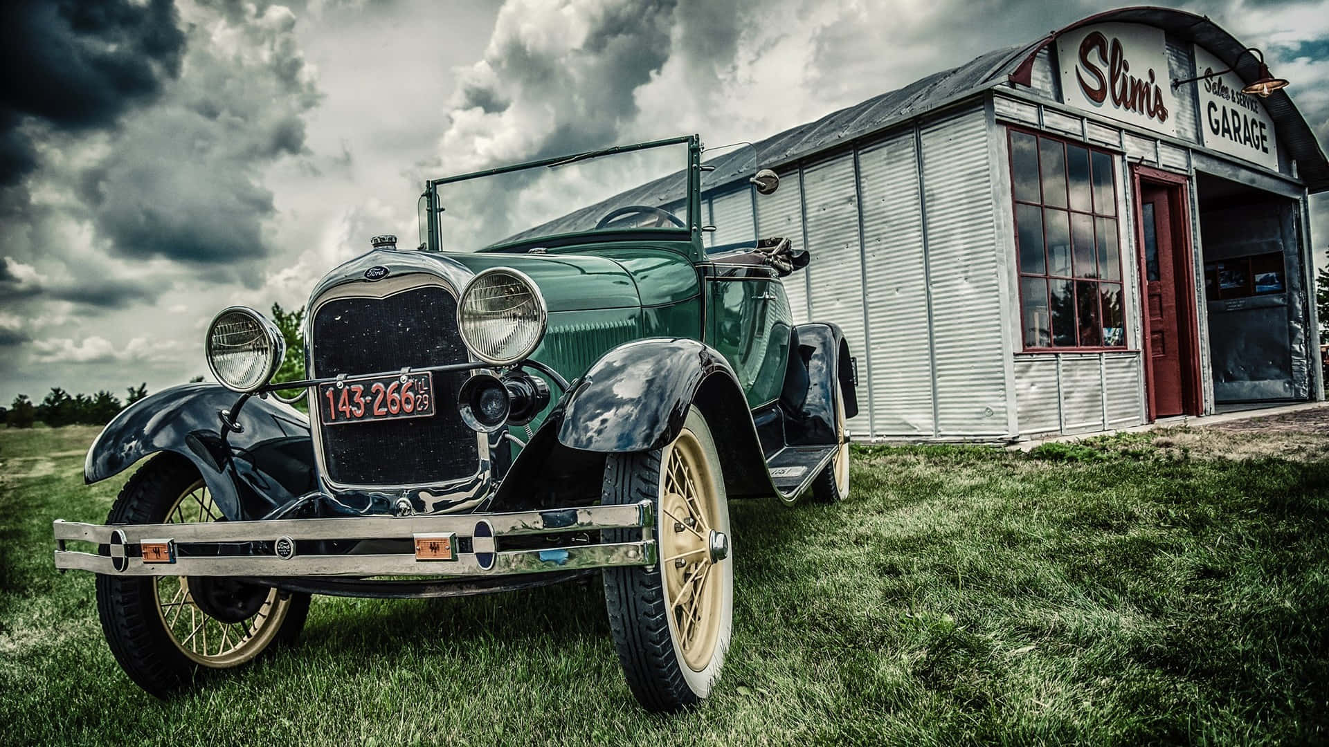 綠色敞篷古董車圖片 壁紙 — 一架復古綠色福特 Model T 停在草地上，前方是飽經風霜的波紋金屬車庫，上方是戲劇性的暴風雲。
