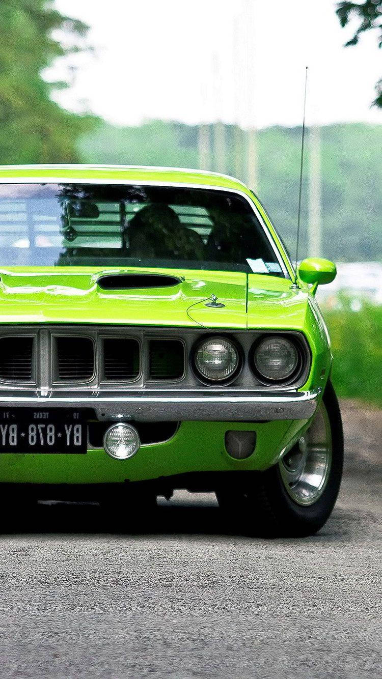 綠色普利茅斯Barracuda汽車 iPhone 壁紙 — 一輛充滿活力的青檸綠色經典肌肉車停在道路上，背景是茂密的綠樹。