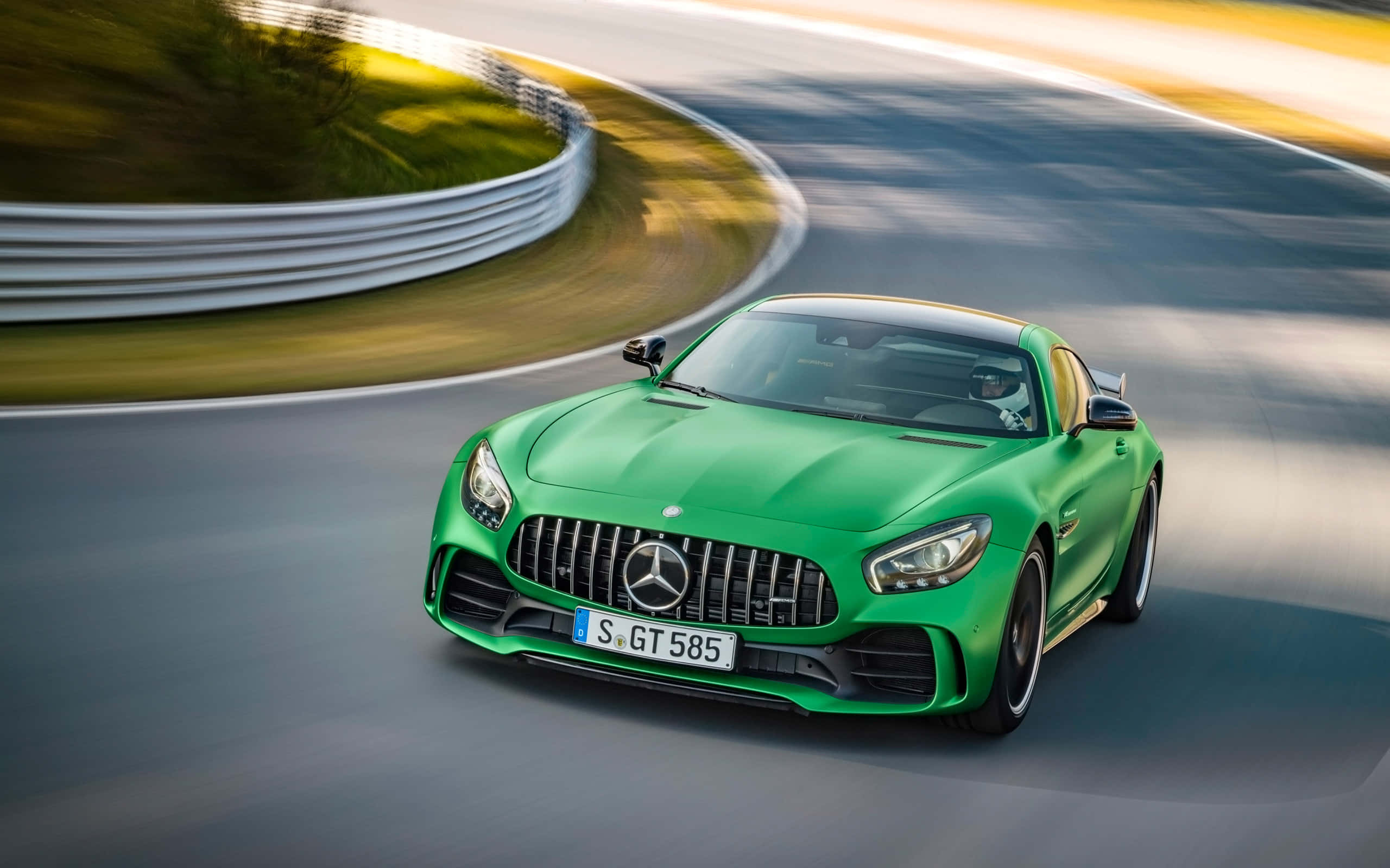 綠色梅賽德斯-AMG GT R 背景 壁紙 — 一輛充滿活力的綠色Mercedes-AMG GT S在彎曲的賽道上奔馳，帶有模糊的動態和金色的陽光。